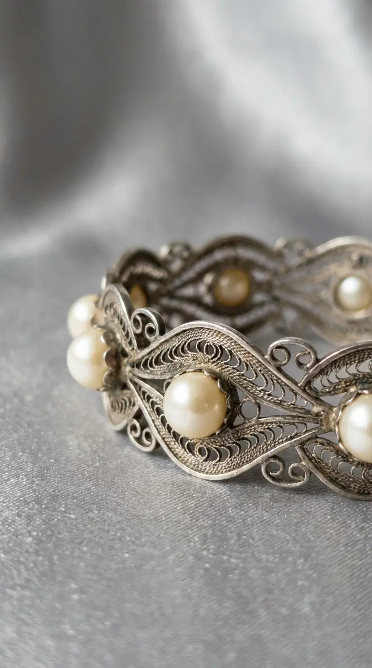 Vintage silver filigree bangle bracelet featuring cream-colored pearls, displayed on a shimmering grey silk background.