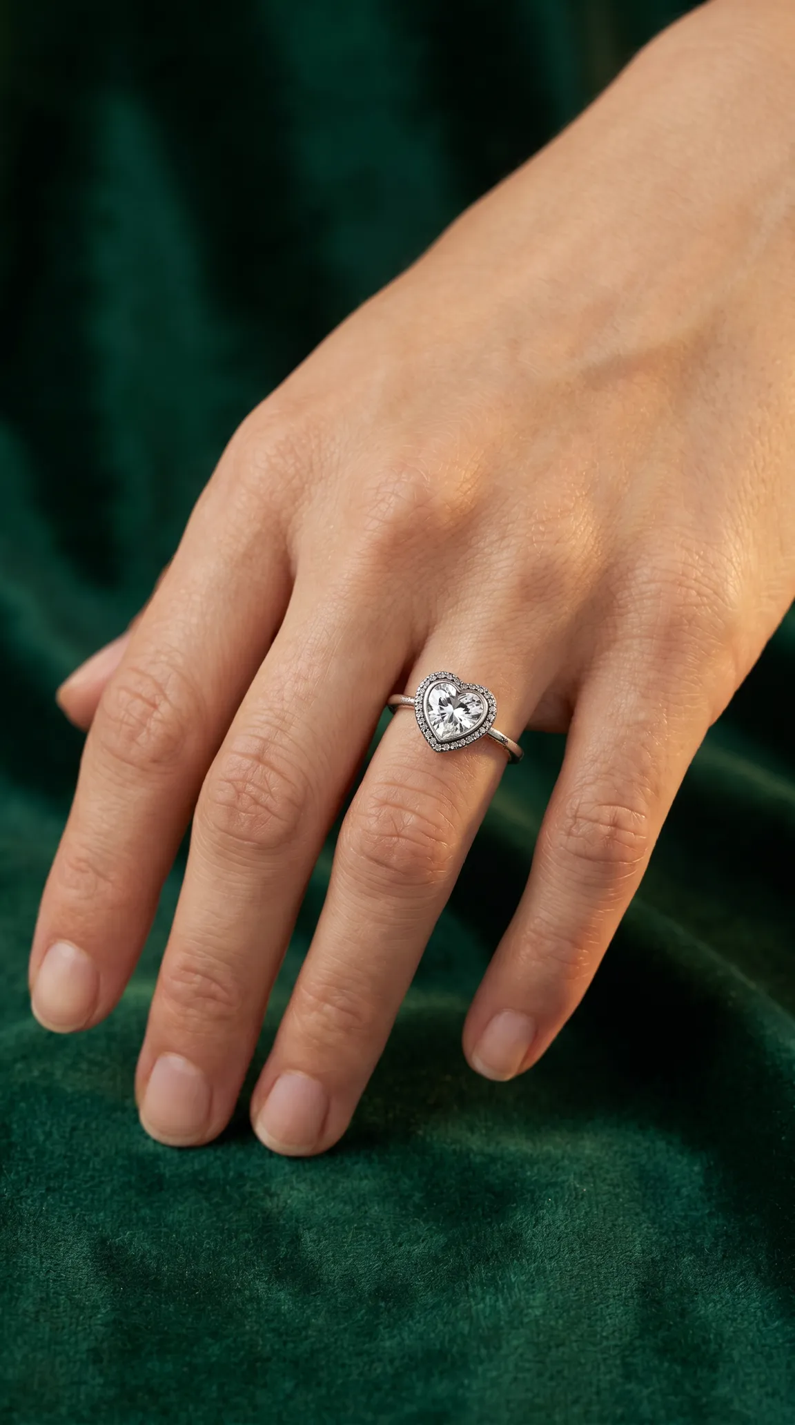 Vintage heart-shaped diamond ring with pave halo on a woman's hand, set against green velvet.