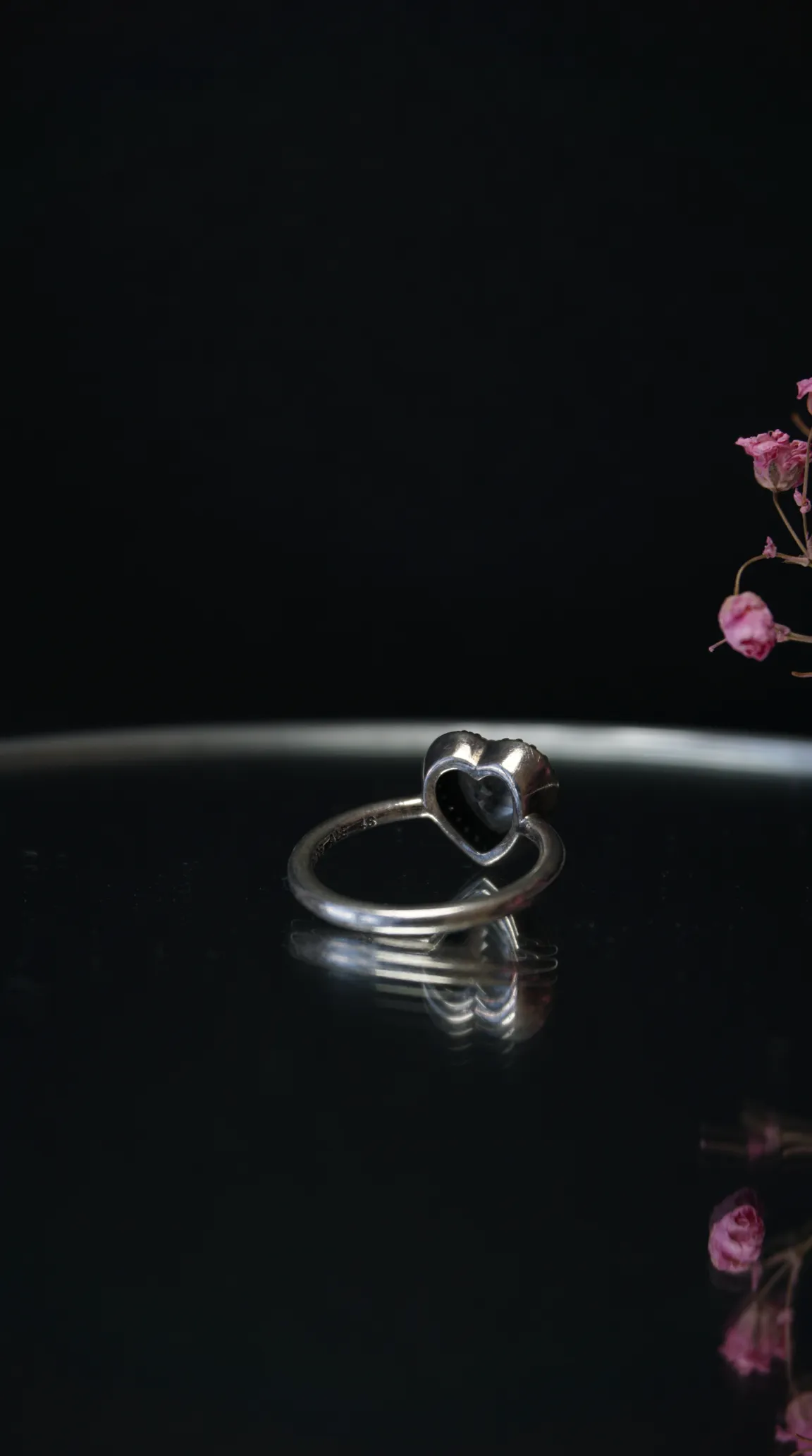 Vintage silver heart ring with black gemstone on a reflective surface.