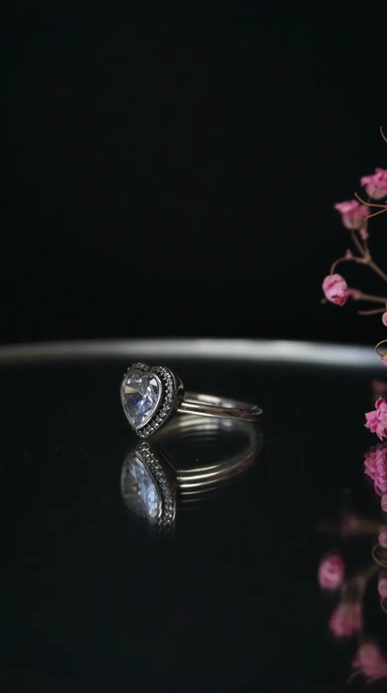 Vintage sterling silver heart-shaped clear gemstone ring with diamond halo and reflection on dark background.