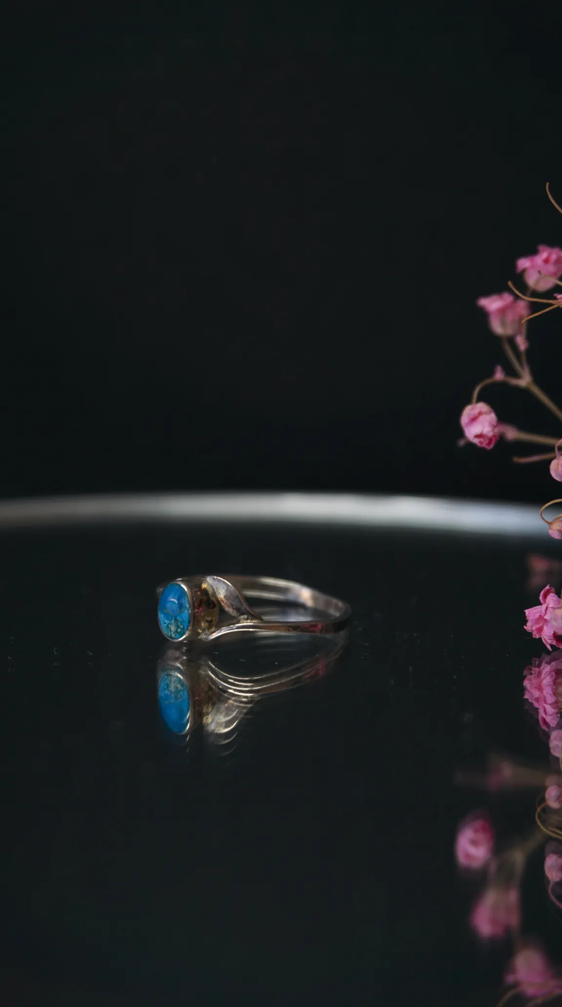 Vintage silver ring with oval blue turquoise gemstone on dark reflective surface with pink flowers