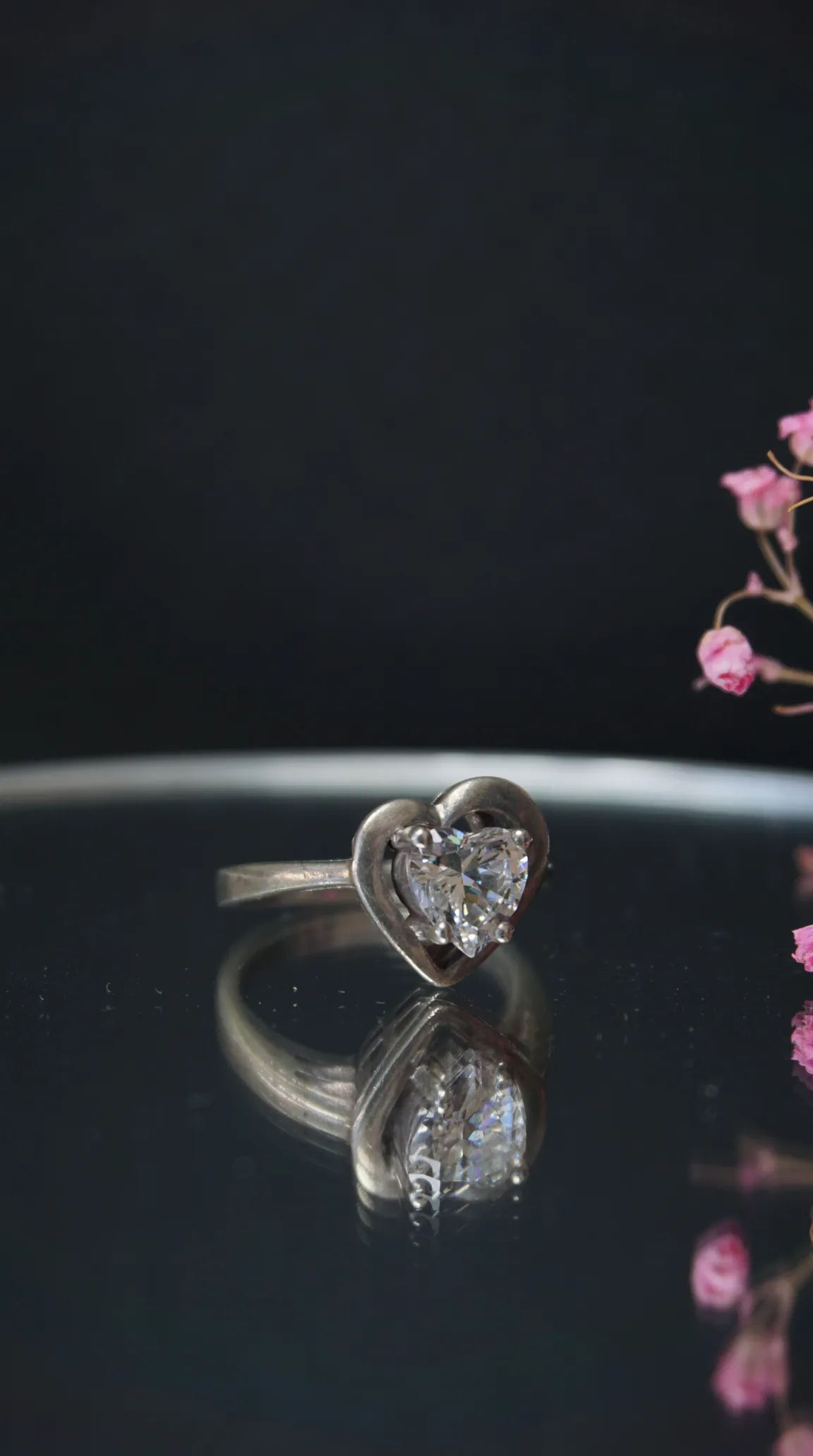 Vintage sterling silver ring with heart-shaped clear gemstone, reflected on a dark surface.