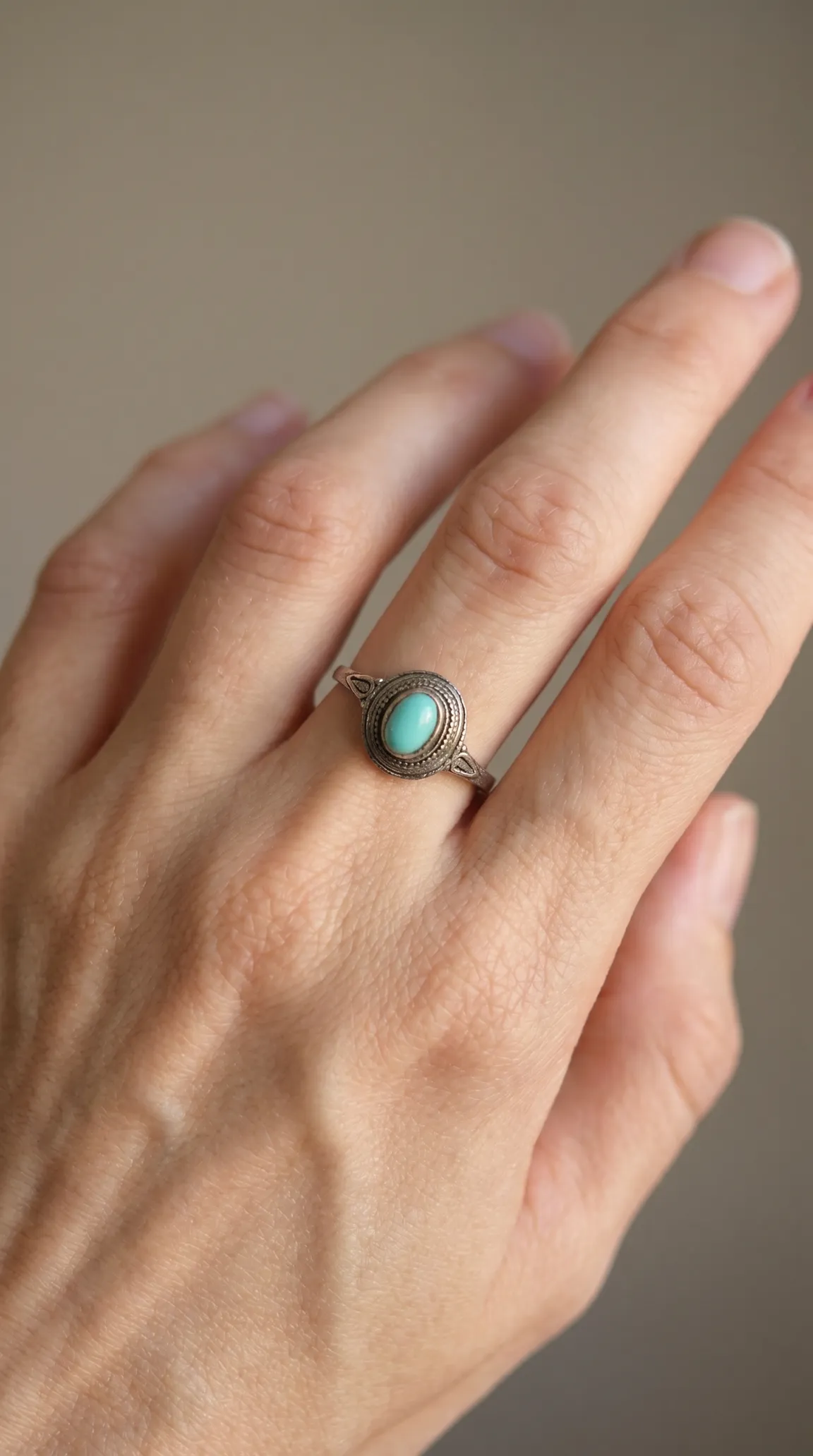Vintage sterling silver ring with oval turquoise gemstone and ornate bezel on a hand.