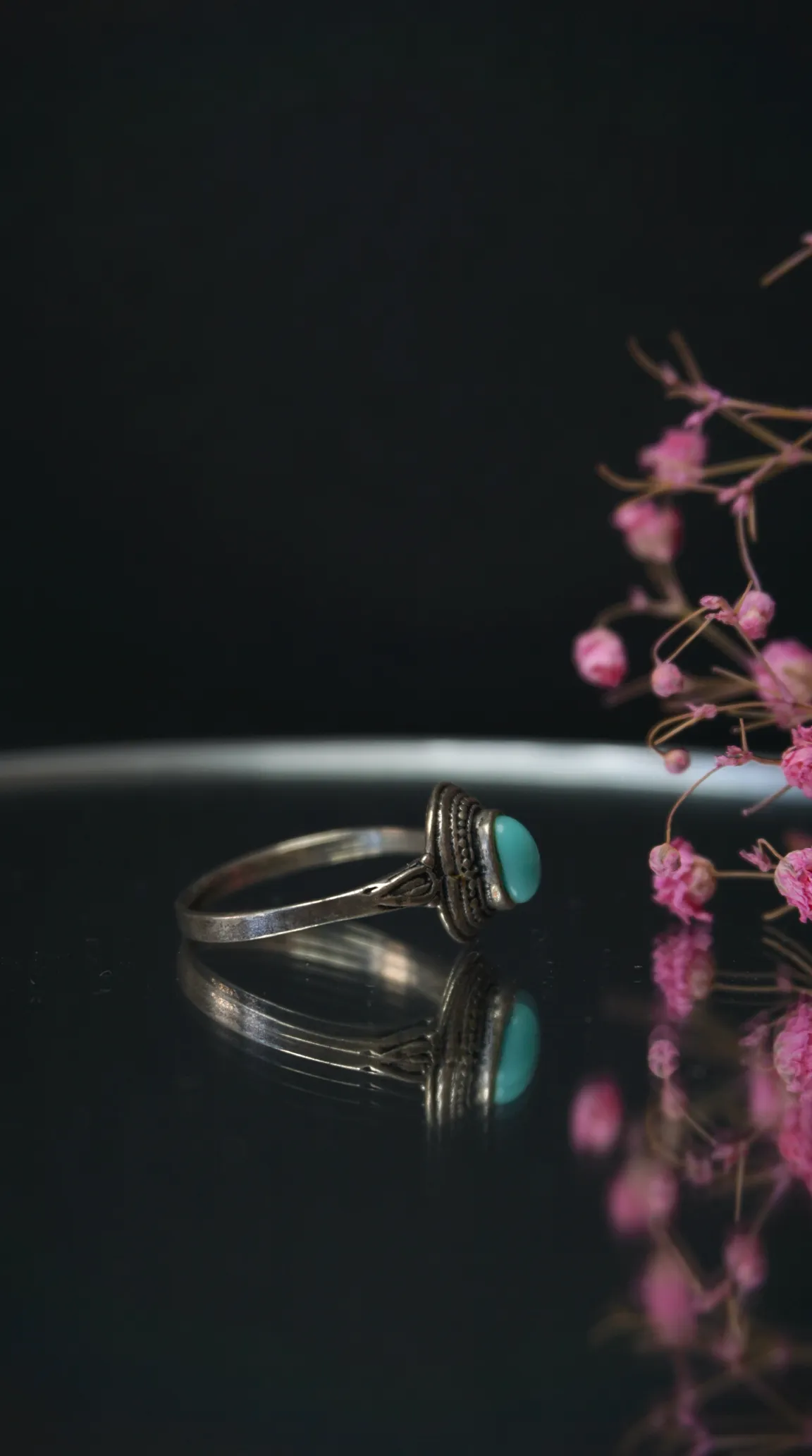 Vintage silver ring with oval turquoise gemstone and intricate band on a dark reflective surface.