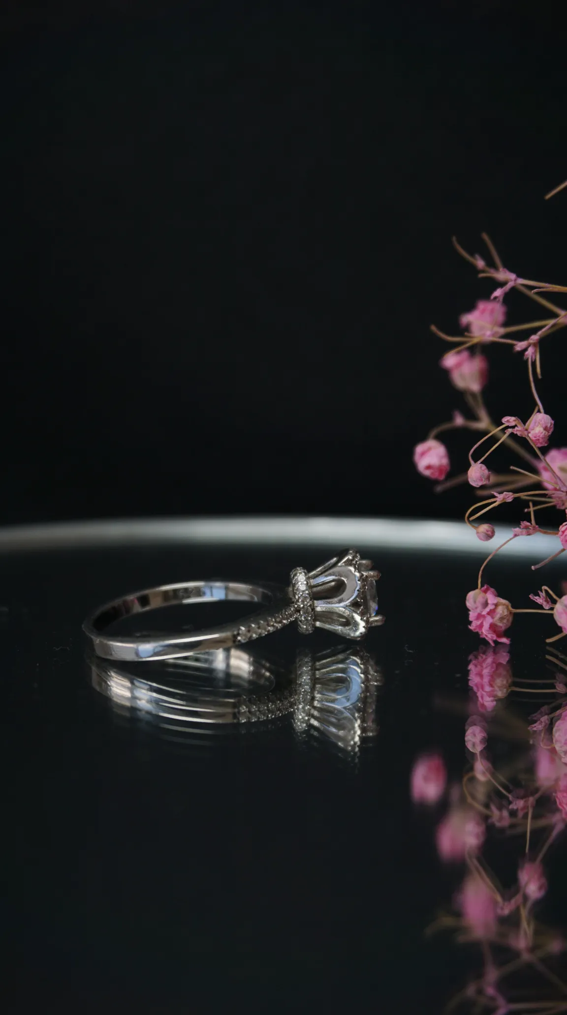 Vintage sterling silver ring with large clear gemstone and pave accent stones, reflecting on a dark surface next to dried pink flowers.