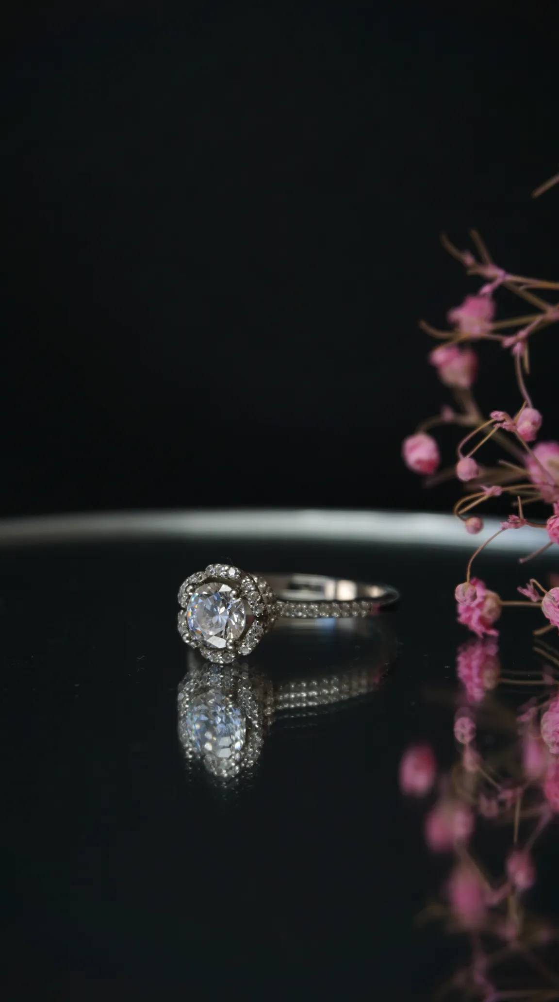 Vintage silver diamond halo ring with pave band, reflecting on dark surface, elegant antique jewelry.