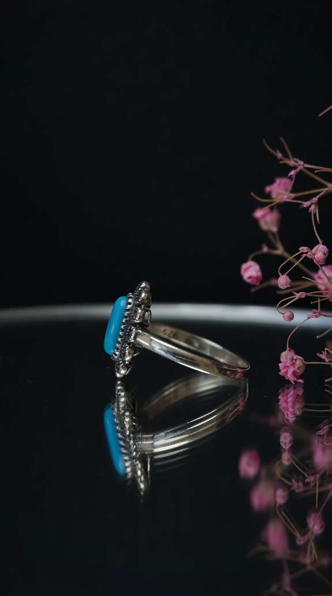 Vintage 925 sterling silver ring with oval blue turquoise gemstone and decorative beaded bezel, on a reflective surface.