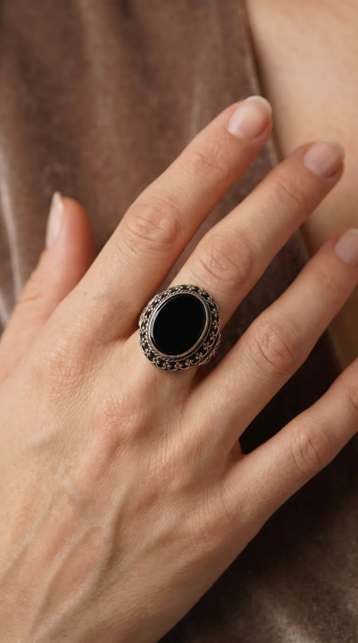 Vintage ornate sterling silver ring with oval black onyx gemstone on a woman's hand.