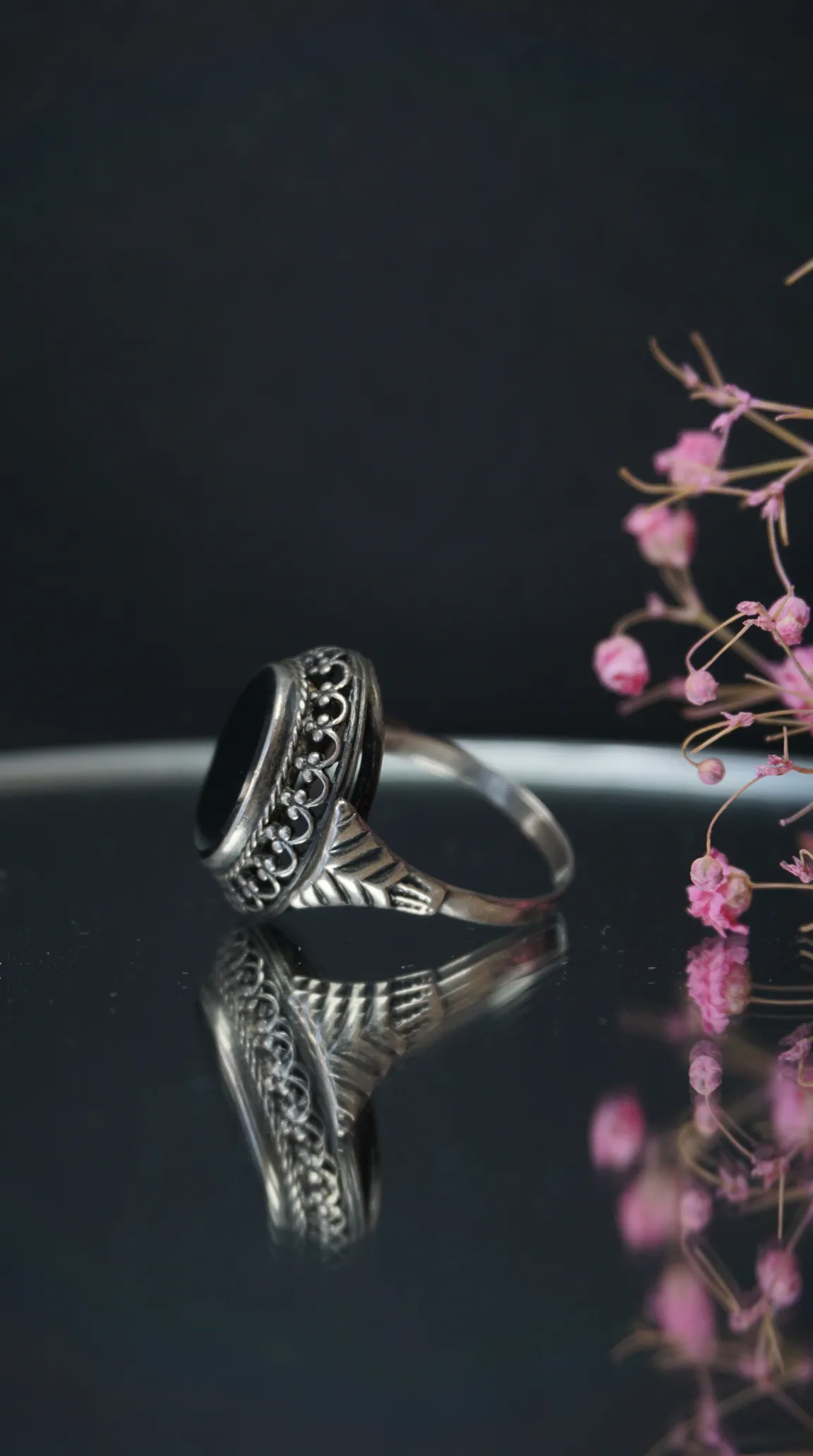 Vintage sterling silver ring with black onyx gemstone, ornate filigree details, and a reflective surface.