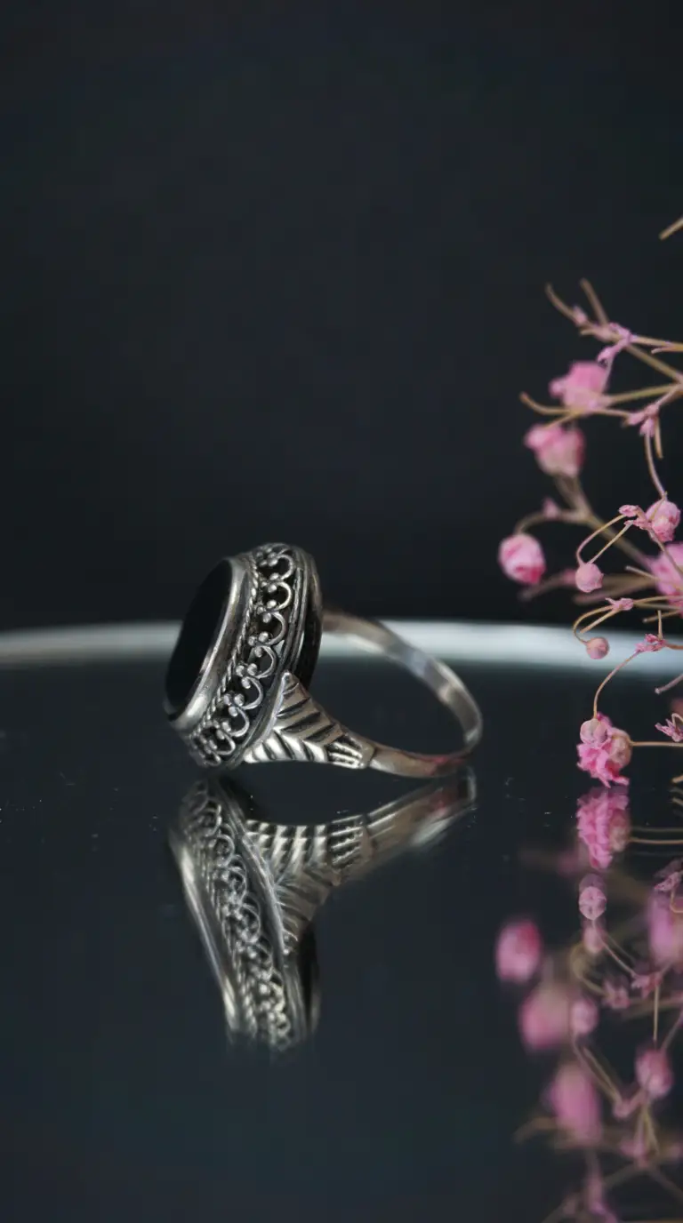 Vintage sterling silver ring with black onyx gemstone, ornate filigree details, and a reflective surface.