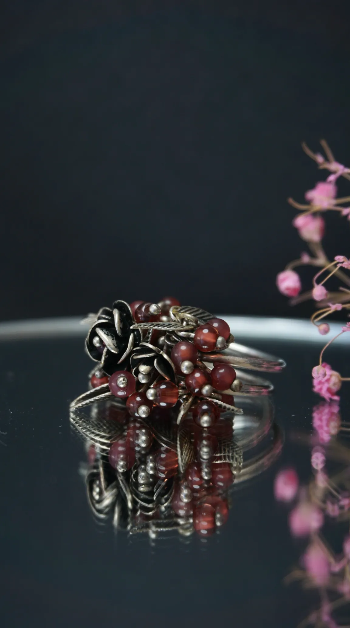 Vintage oxidized silver ring with dark red bead clusters and detailed floral rose and leaf designs.