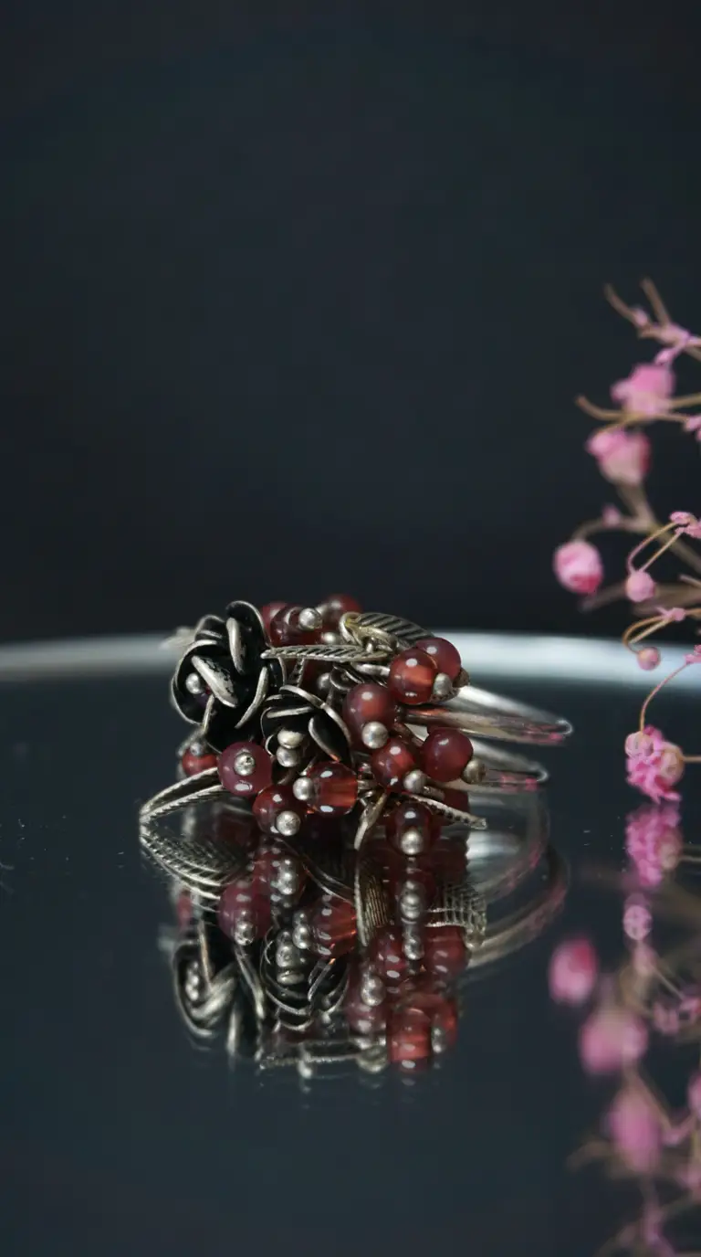 Vintage oxidized silver ring with dark red bead clusters and detailed floral rose and leaf designs.