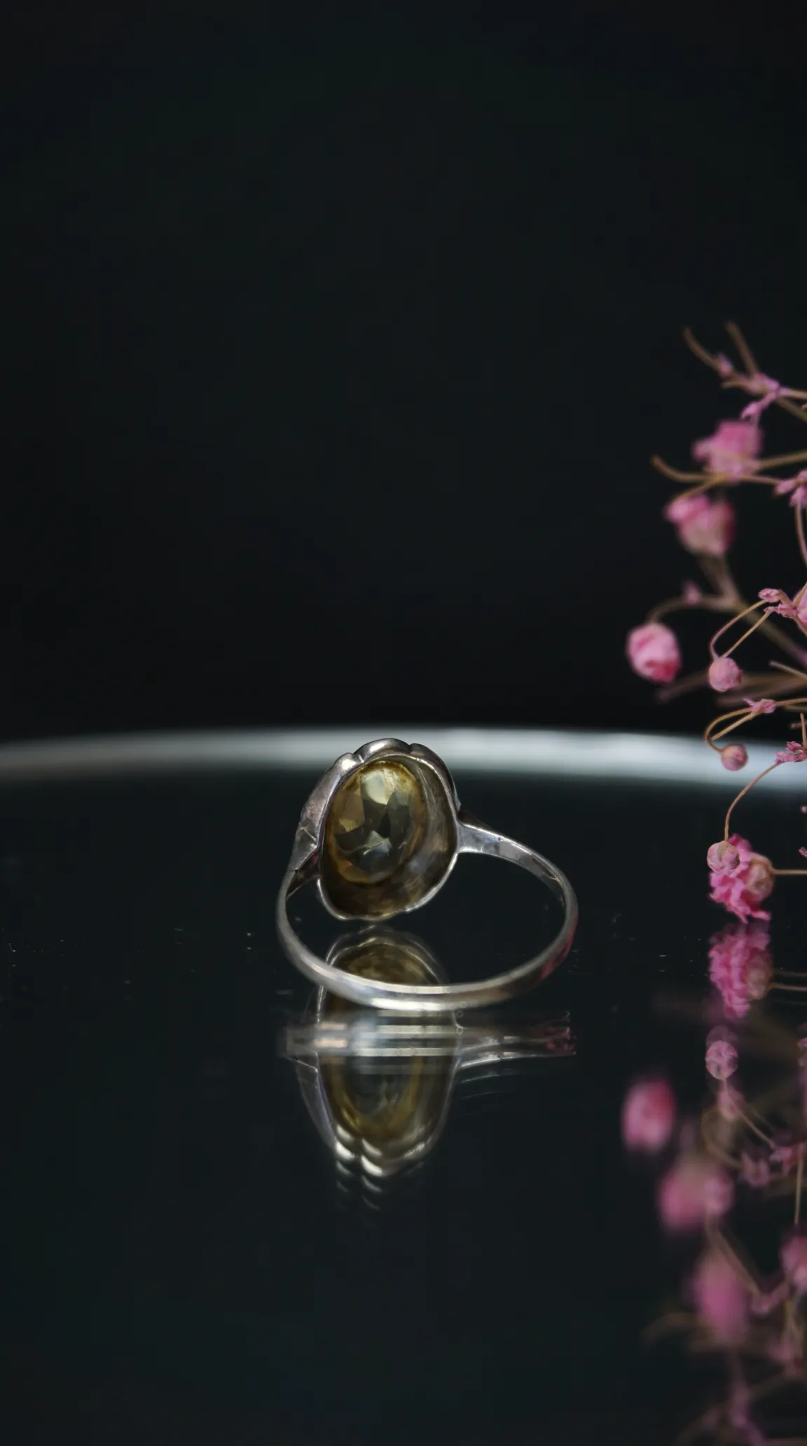 Vintage silver ring with faceted yellow gemstone on reflective black surface