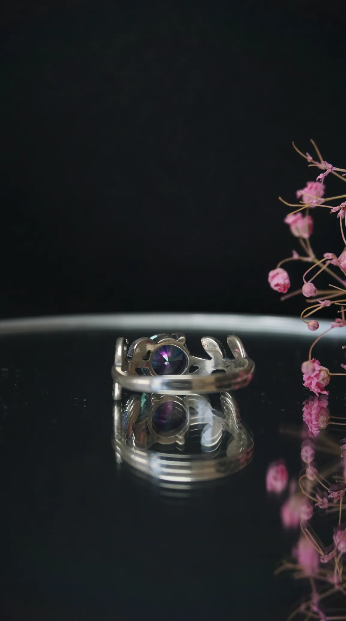 Vintage sterling silver ring with oval mystic topaz gemstone on dark reflective surface.