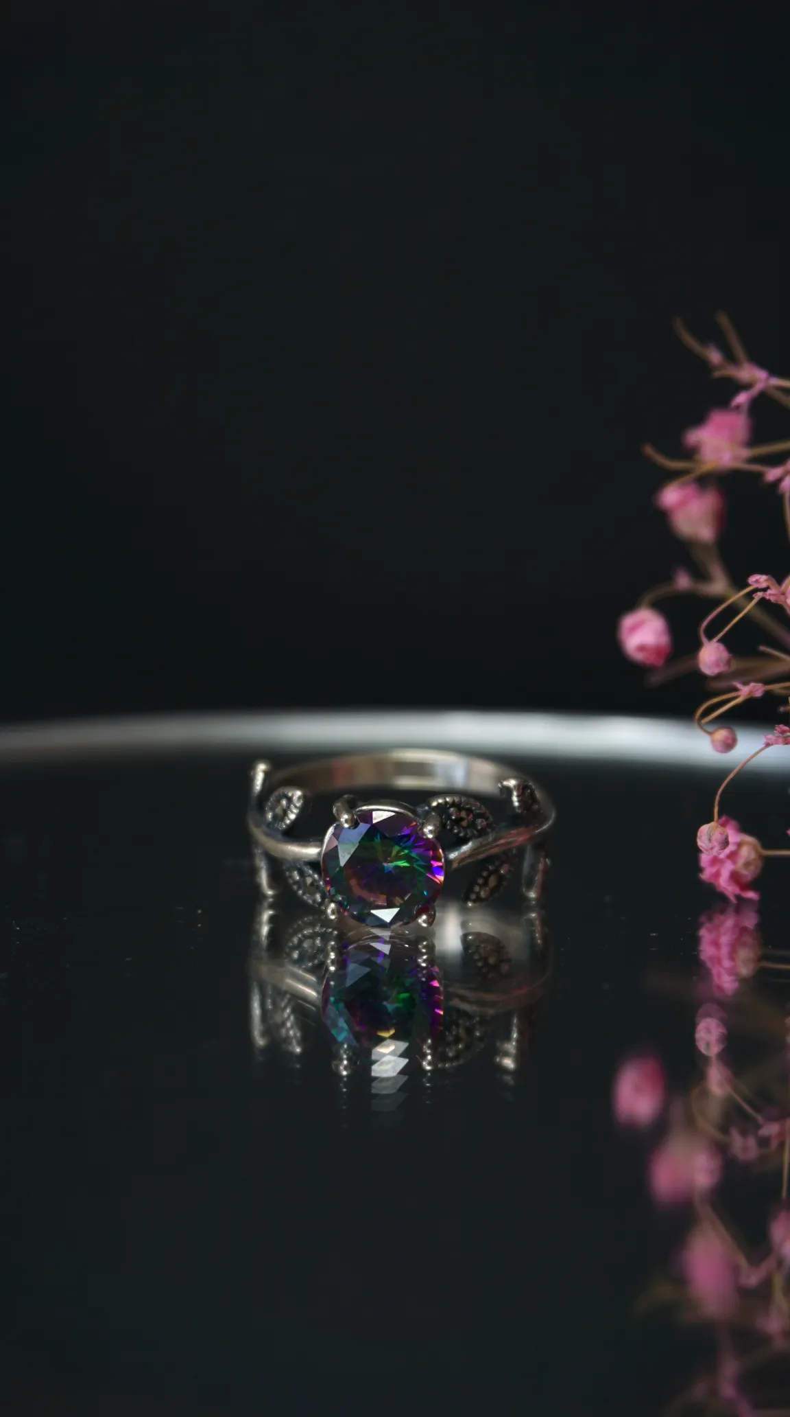 Vintage silver ring with rainbow mystic topaz gemstone, ornate design, antique jewelry on dark reflective surface.