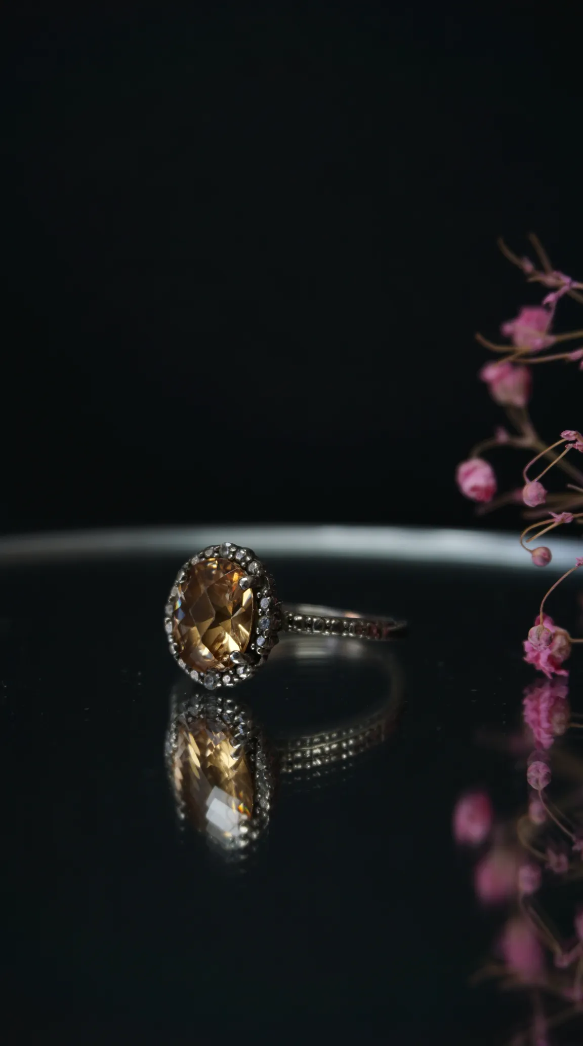 Vintage oval golden topaz or citrine halo ring with silver-toned band, reflecting on dark surface.