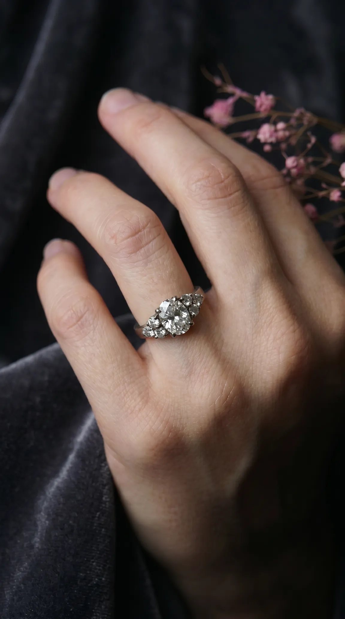 Vintage oval diamond cluster ring on a hand against dark velvet.
