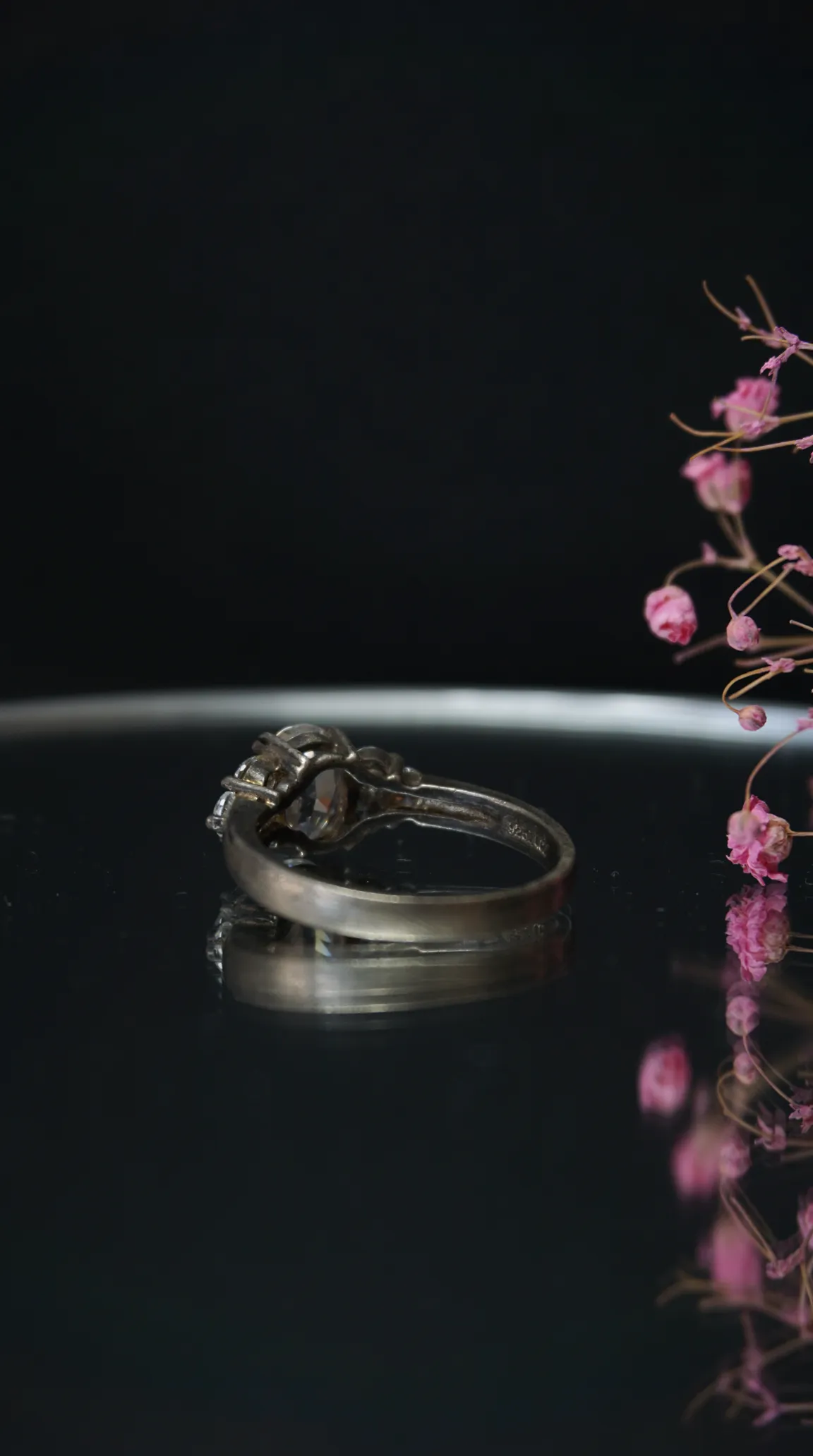 Vintage sterling silver ring with clear round gemstone and accent stones on black reflective surface.