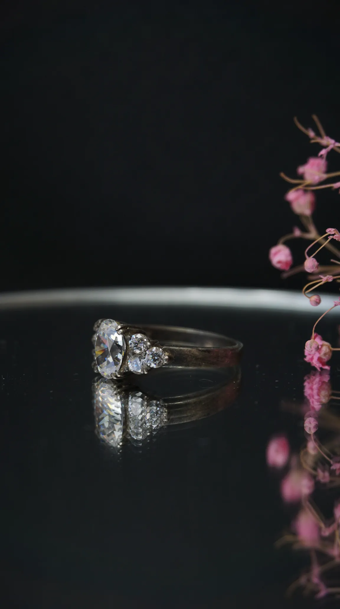 Vintage silver oval clear gemstone ring with accent stones, reflecting on dark surface. Antique jewelry.