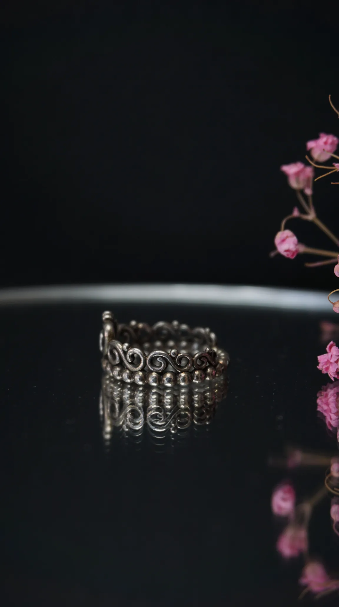 Vintage ornate silver scroll ring and beaded band reflecting on dark surface.