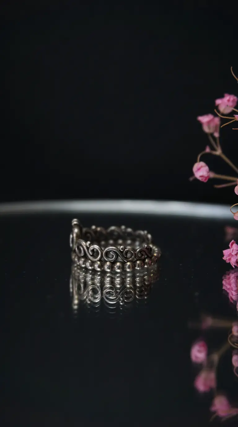 Vintage ornate silver scroll ring and beaded band reflecting on dark surface.