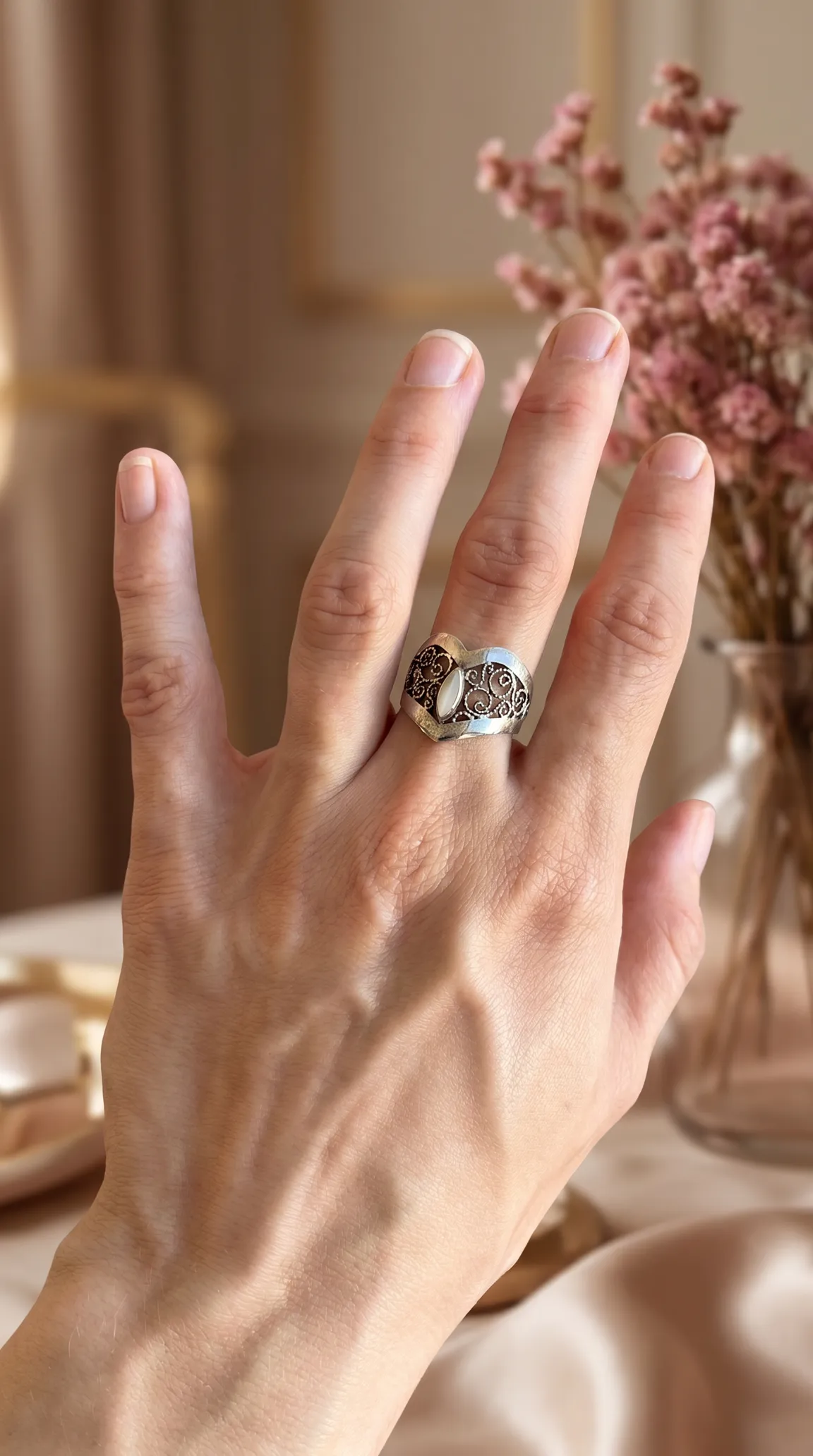 Ornate vintage silver filtone filigree ring with oval mother-of-pearl stone worn on a hand.
