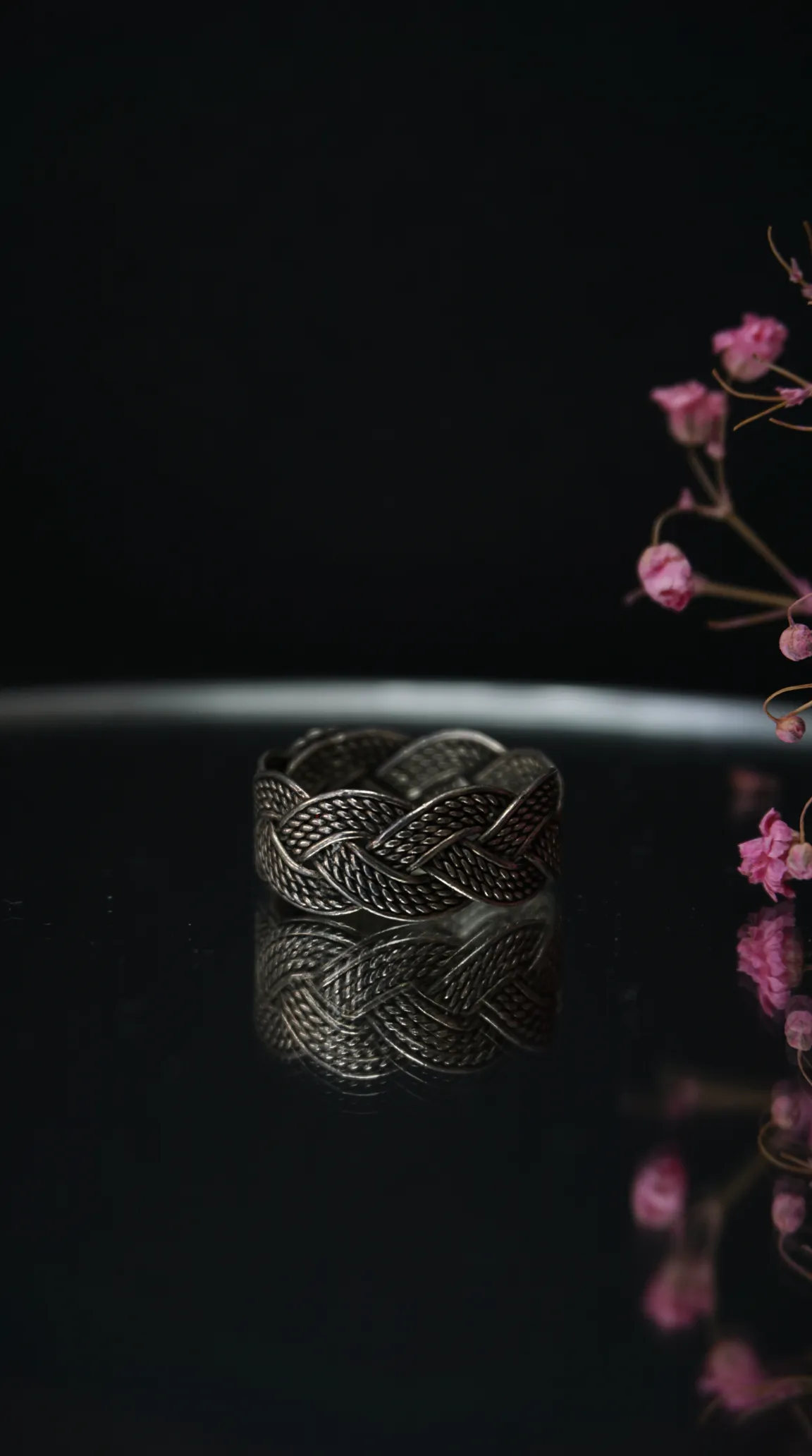 Vintage silver braided ring with woven design on a reflective surface