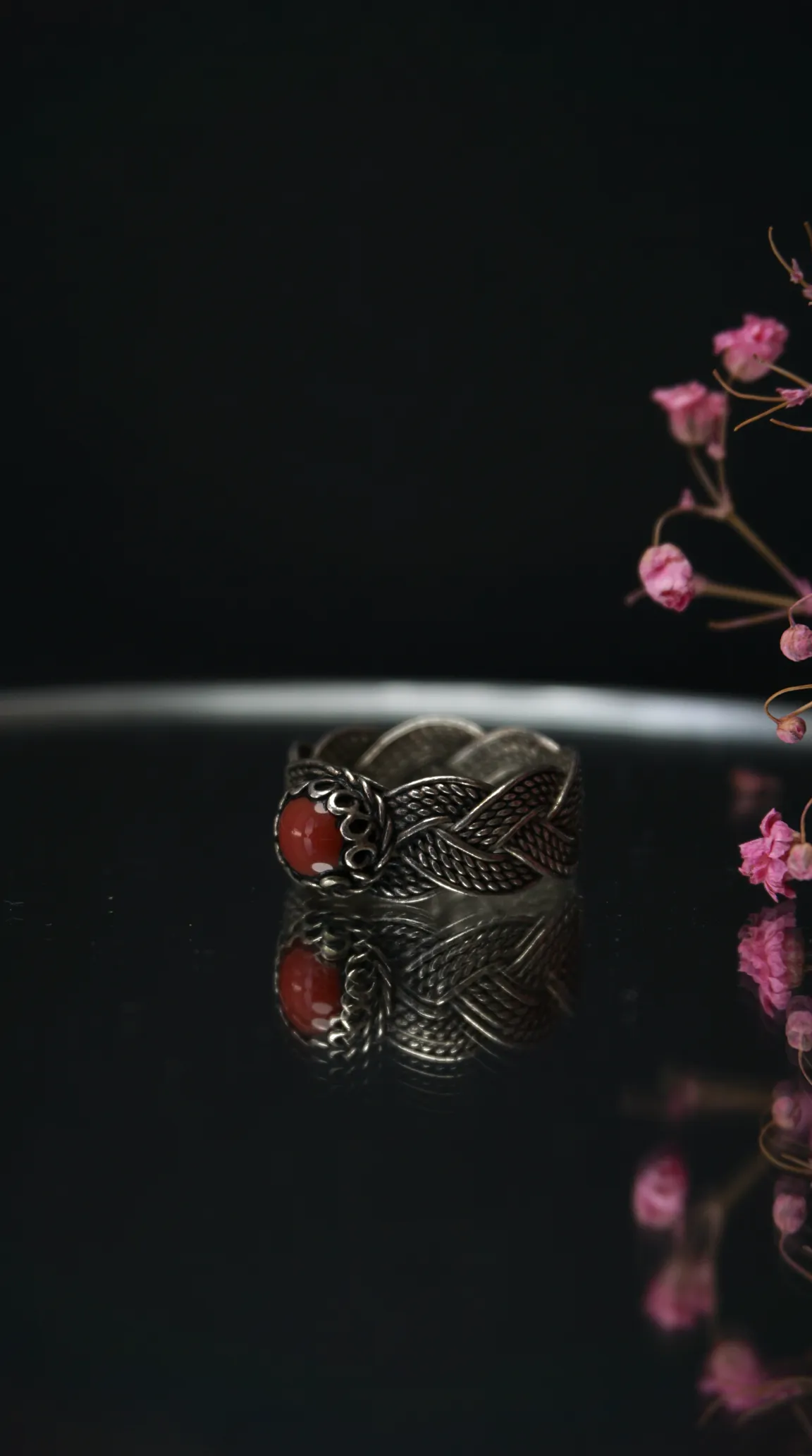 Vintage sterling silver ring with braided band and round red coral gemstone, on a reflective surface.
