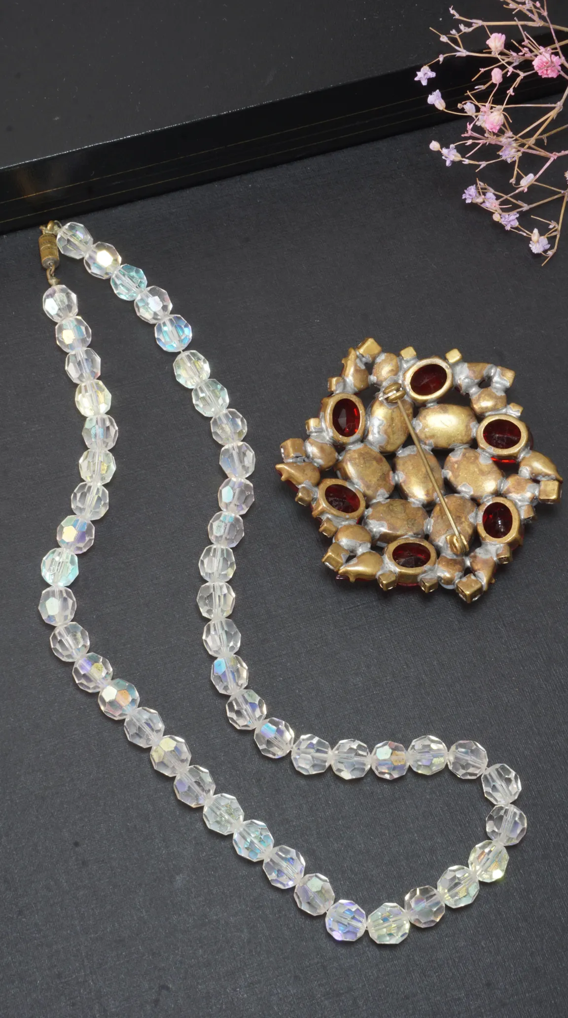 Vintage iridescent faceted crystal bead necklace and vintage gold tone brooch with red oval cabochon stones, showing the pin back.