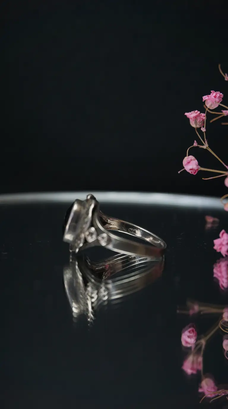 Vintage sterling silver ring with dark oval gemstone on reflective black surface, accented by pink dried flowers.