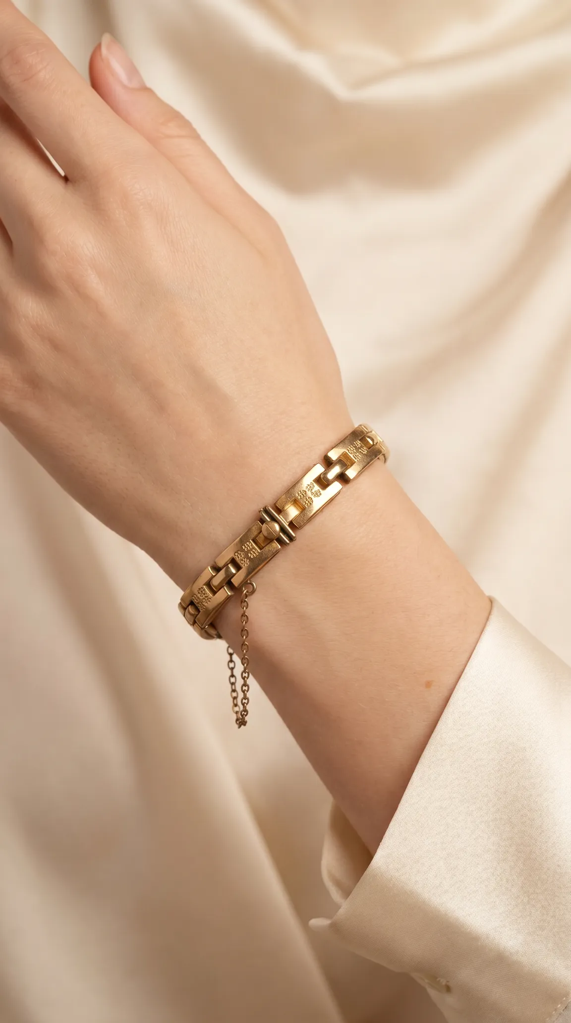 Vintage gold link bracelet with engraved pattern and safety chain on woman's wrist