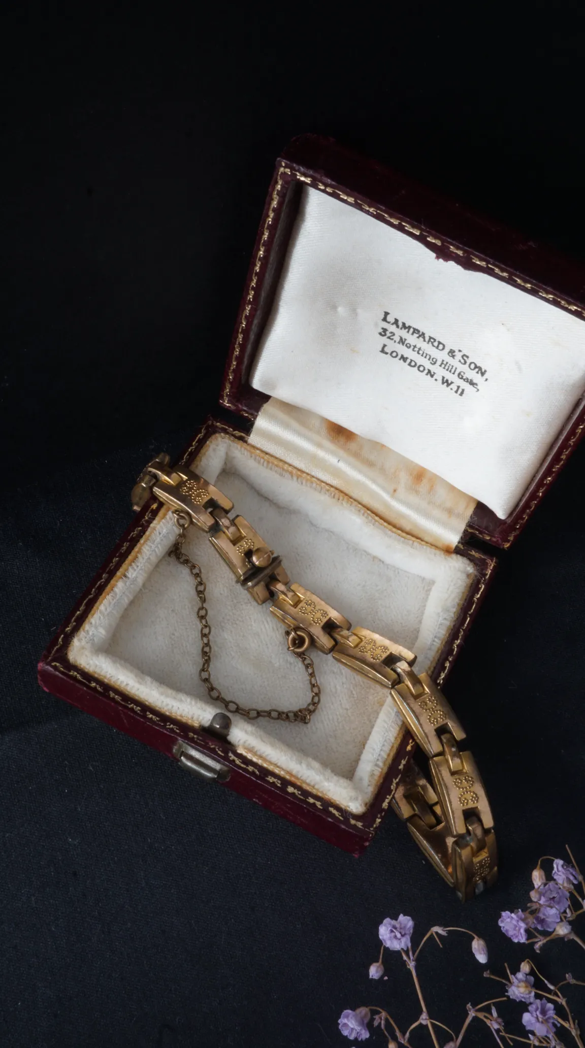 Vintage gold engraved link bracelet with safety chain, presented in an open antique burgundy Lampard & Son London jewelry box.
