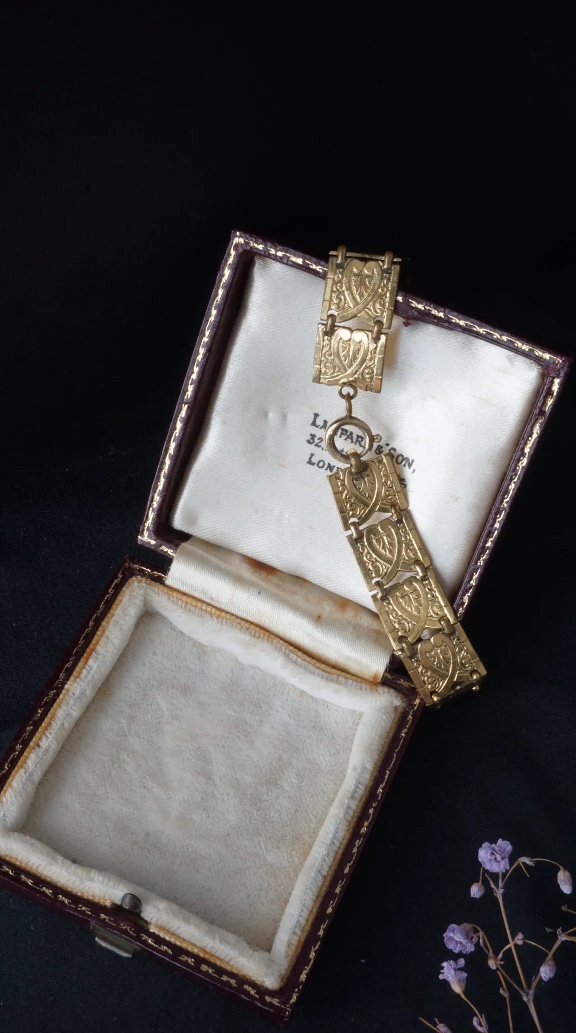 Vintage gold linked bracelet with ornate heart and scroll design, displayed in an antique burgundy jewelry box with cream silk lining.