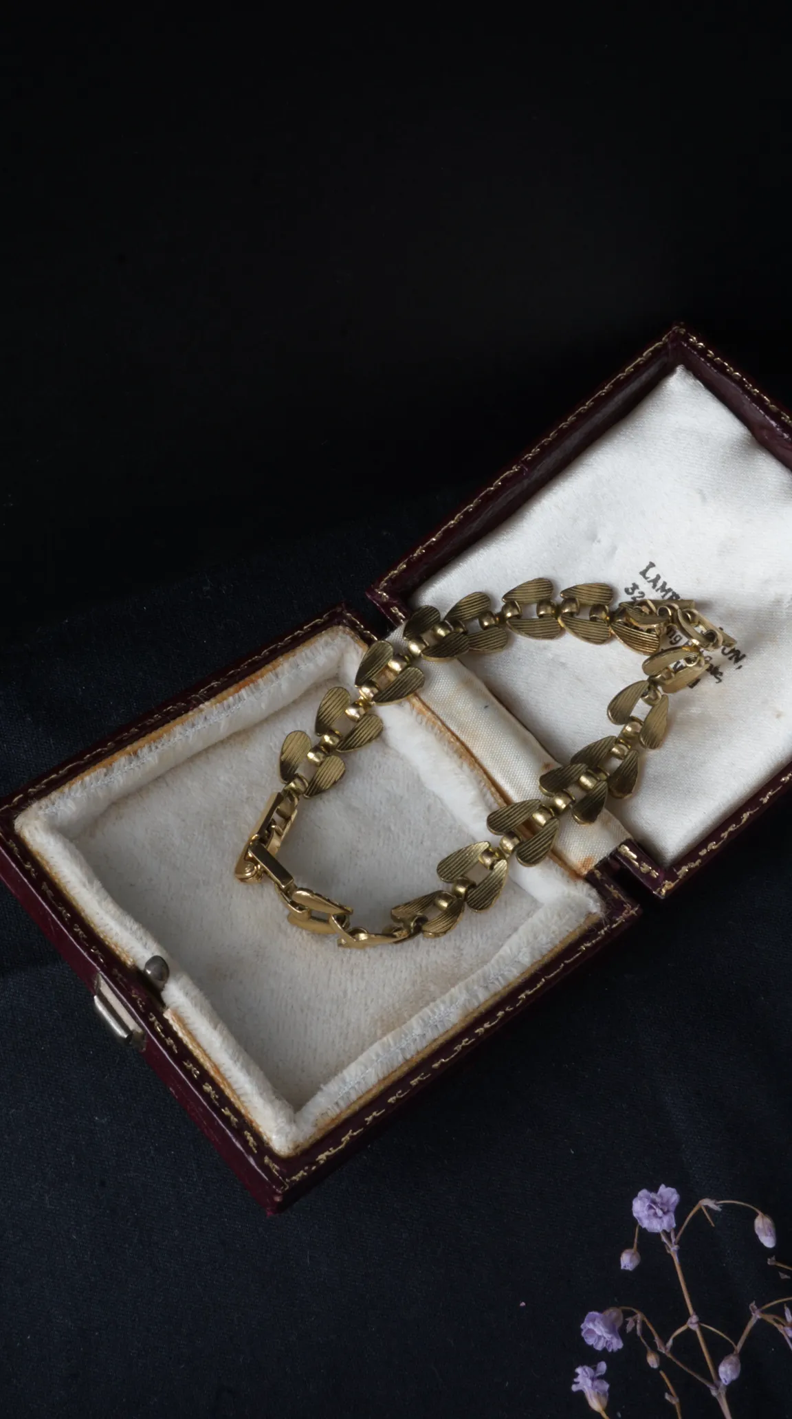 Vintage gold-toned bracelet with textured heart-shaped links in open antique burgundy jewelry box.