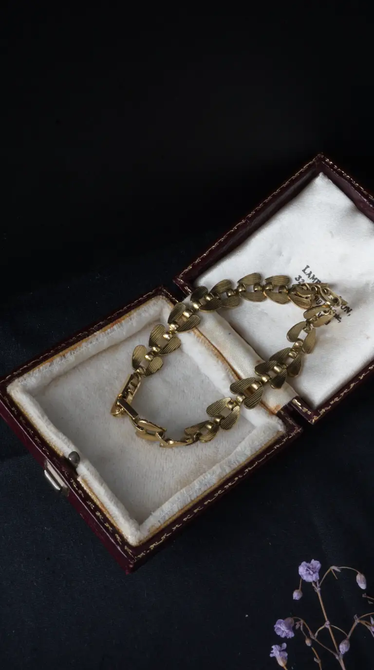 Vintage gold-toned bracelet with textured heart-shaped links in open antique burgundy jewelry box.