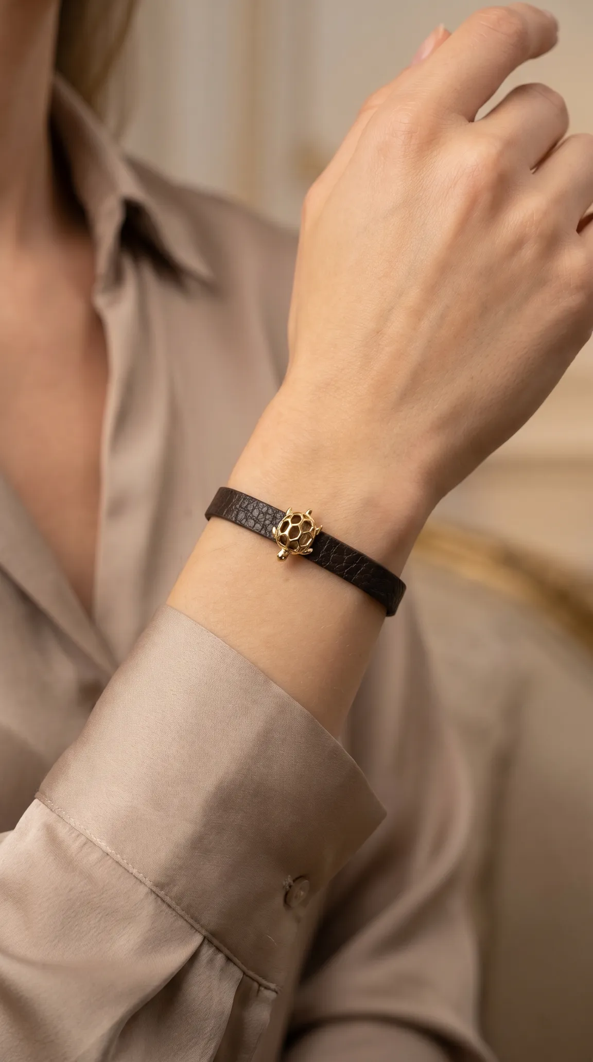 Vintage dark brown leather bracelet with gold honeycomb turtle charm on a woman's wrist.