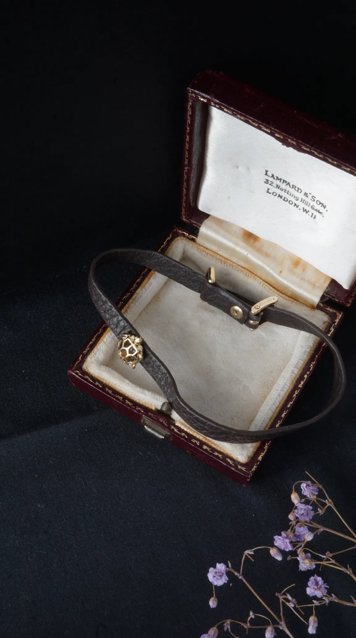 Vintage Fossil dark brown leather bracelet with gold spherical charm, displayed in antique Lampard & Son London jewelry box.