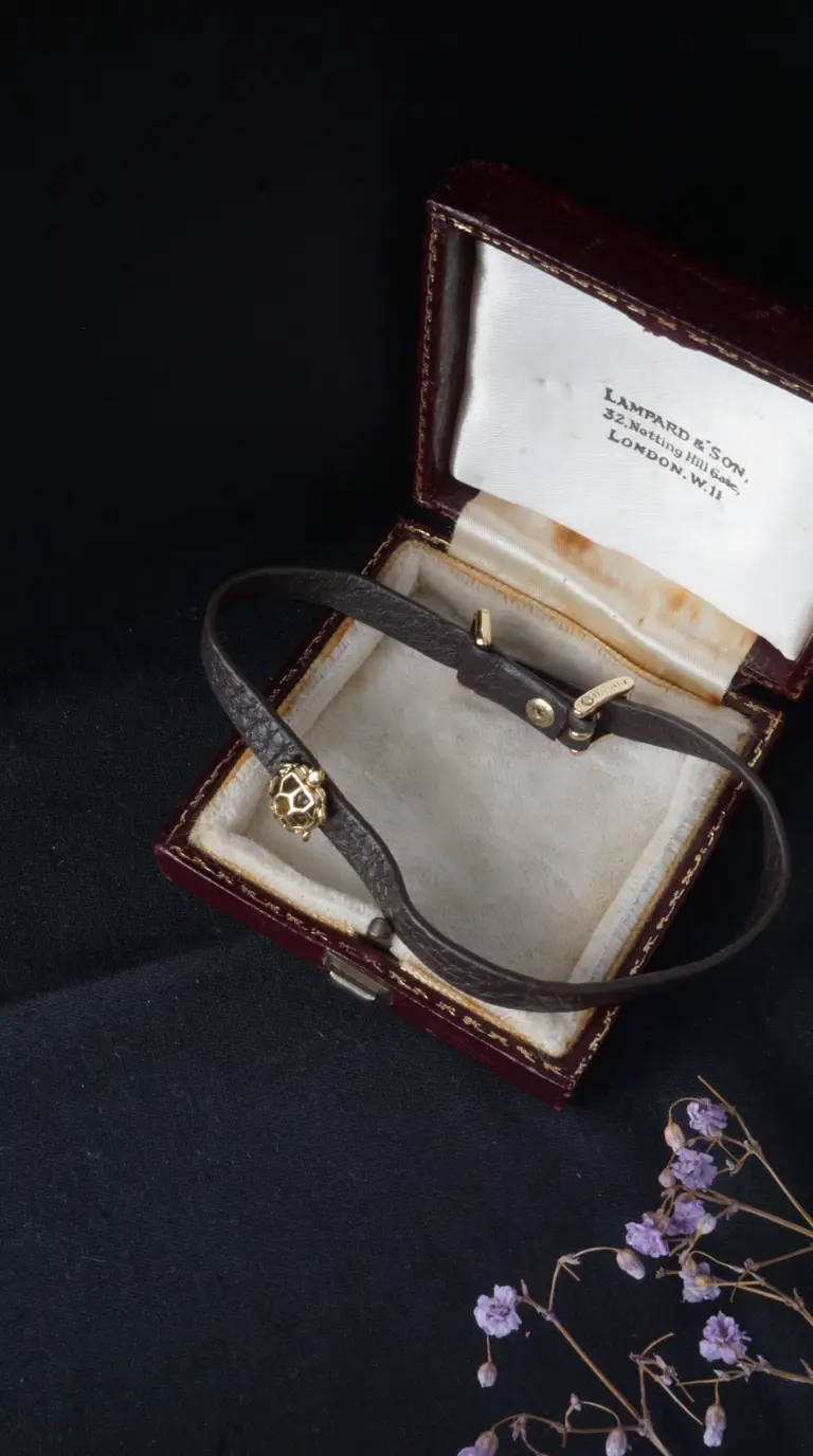 Vintage Fossil dark brown leather bracelet with gold spherical charm, displayed in antique Lampard & Son London jewelry box.