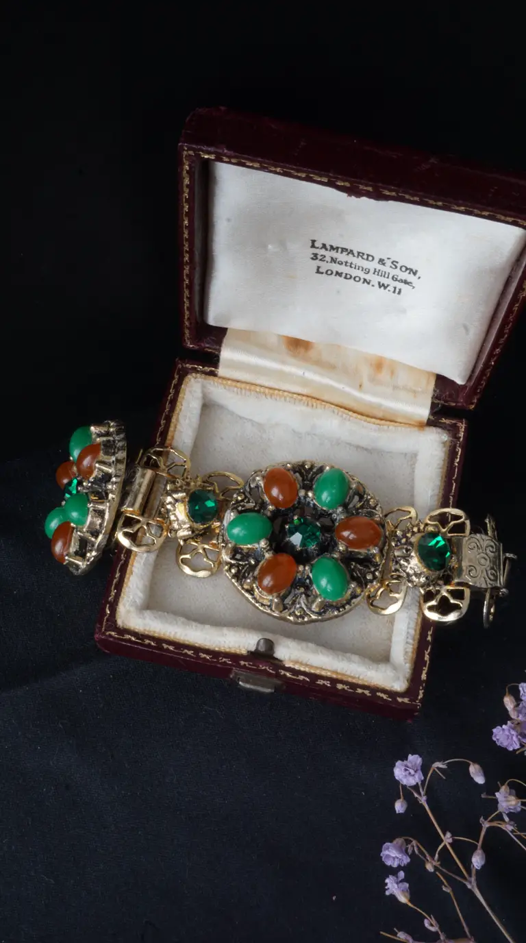 Vintage gold tone ornate bracelet and matching clip-on earrings with emerald green and amber cabochon gemstones, displayed in an open antique burgundy velvet jewelry box from Lampard & Son, London.