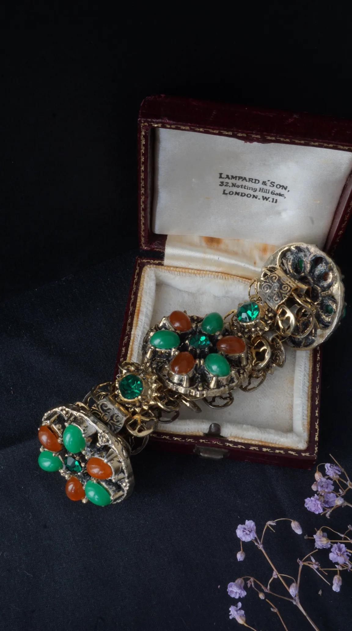 Vintage ornate gold tone bracelet with green and orange cabochon and faceted stones, displayed in a red velvet Lampard & Son London jewelry box.
