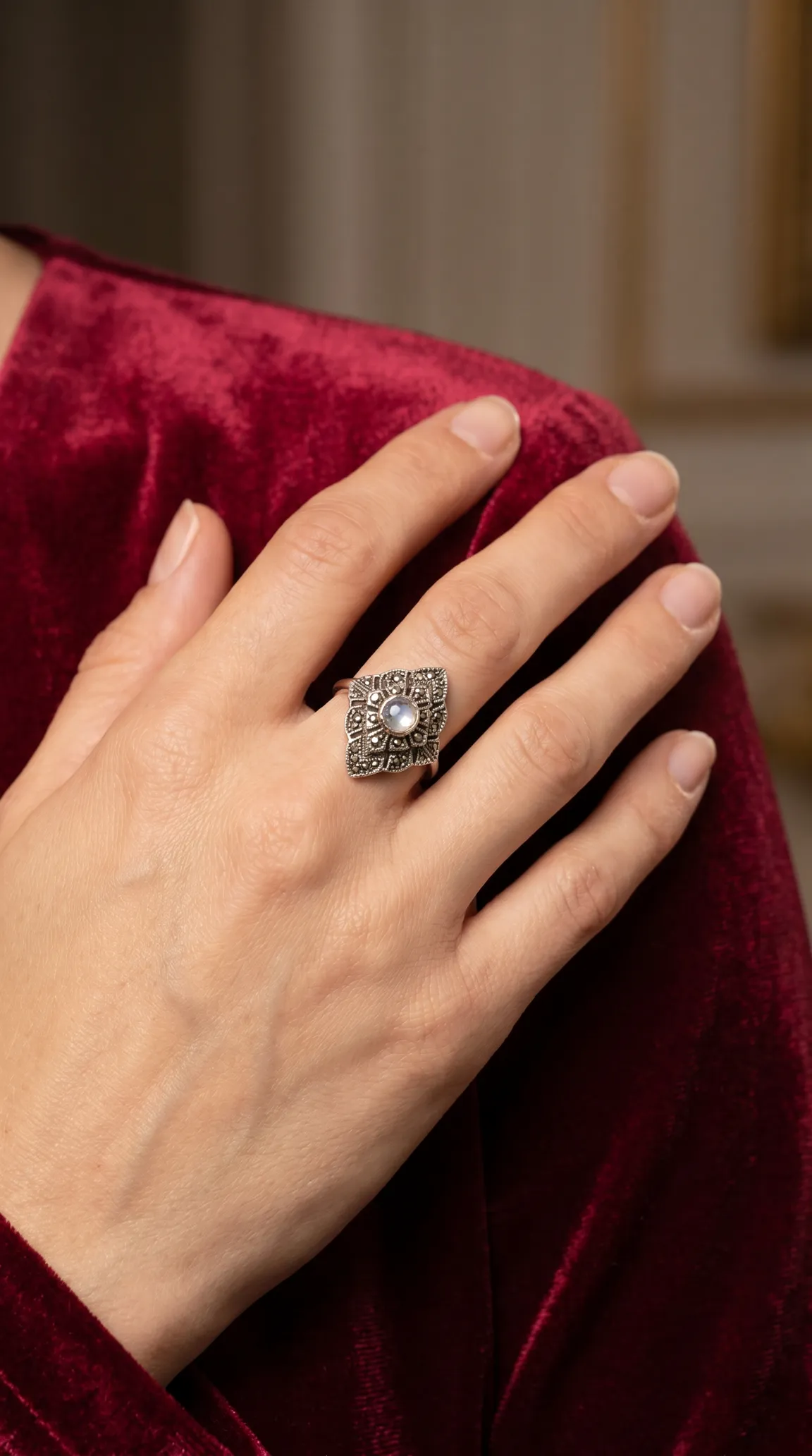 Vintage Art Deco marcasite and moonstone ring on a woman's hand wearing red velvet.