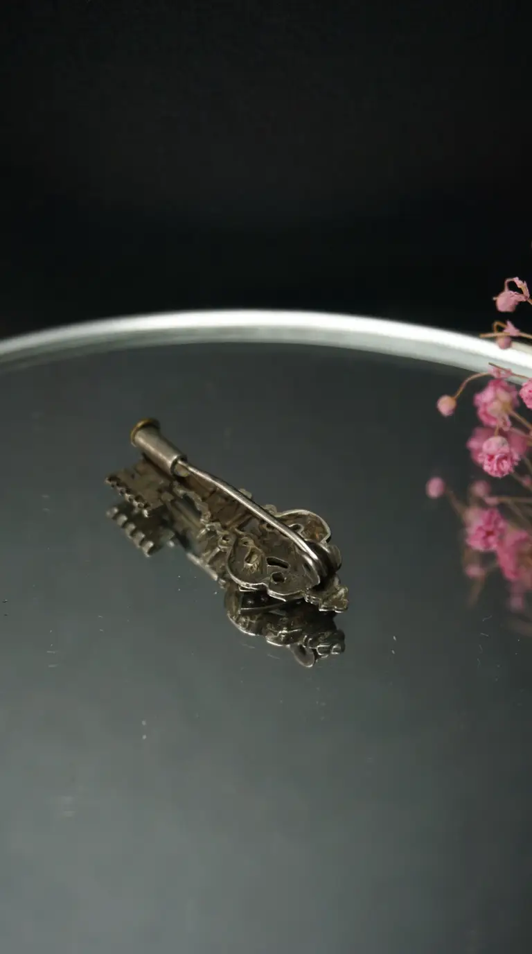 Vintage ornate silver key brooch on reflective surface