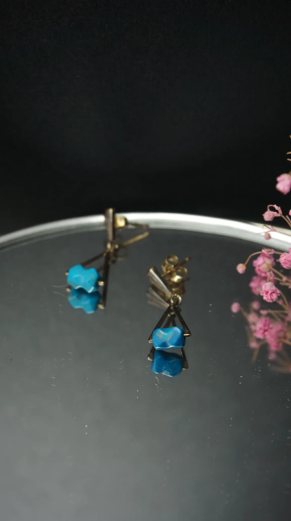 Vintage gold-tone dangle earrings with blue turquoise nugget beads on a reflective surface.