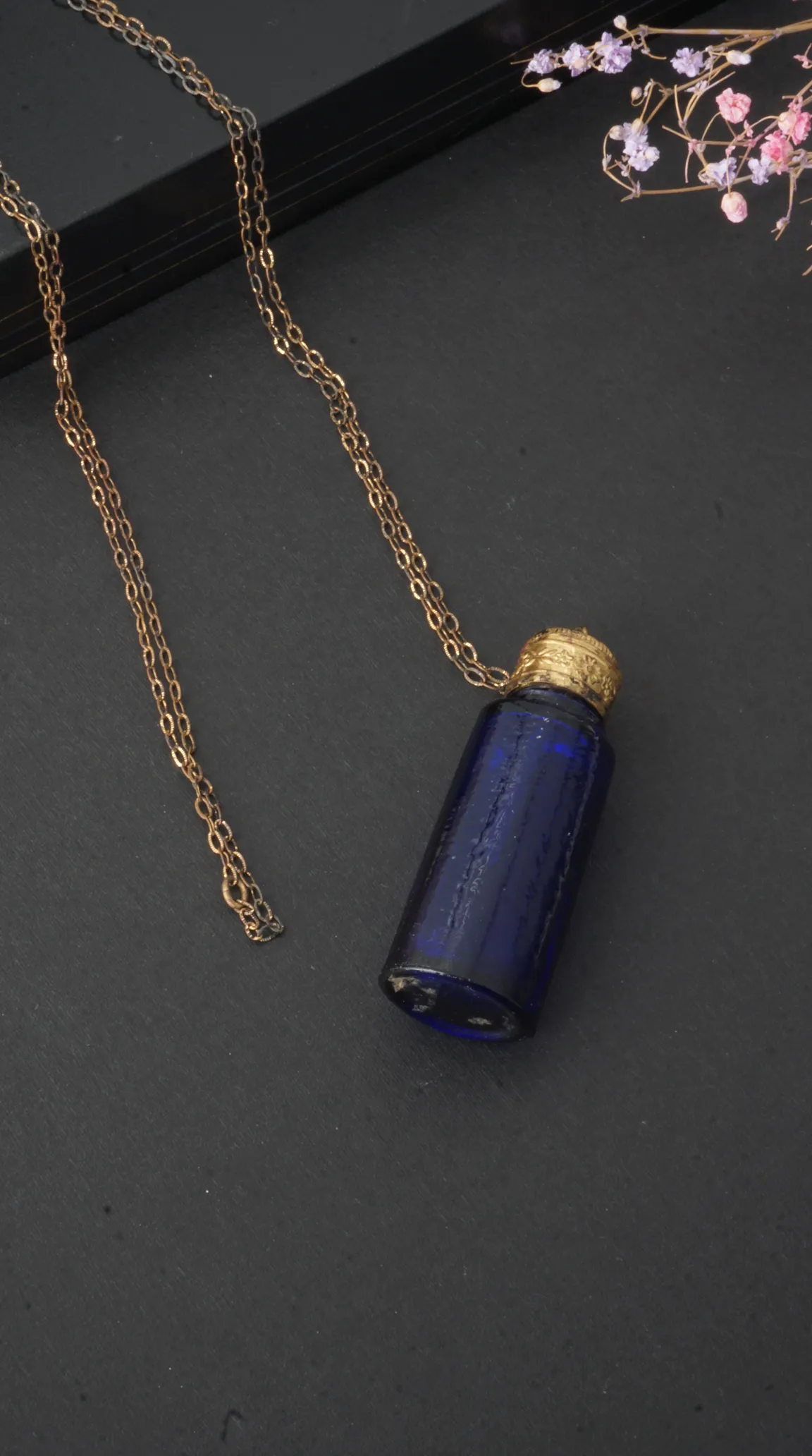 Vintage dark blue glass bottle pendant necklace with ornate gold cap and delicate gold chain.