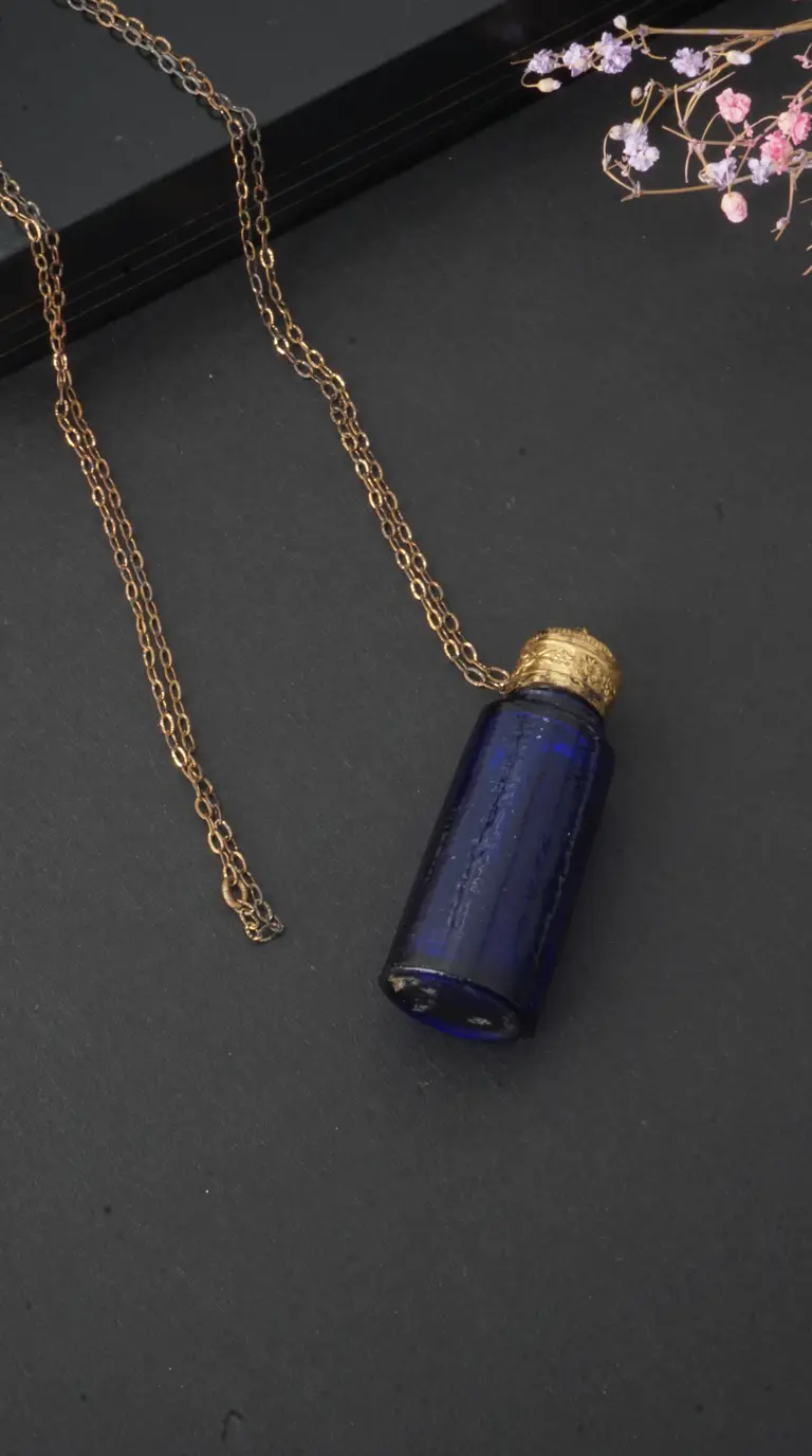 Vintage dark blue glass bottle pendant necklace with ornate gold cap and delicate gold chain.