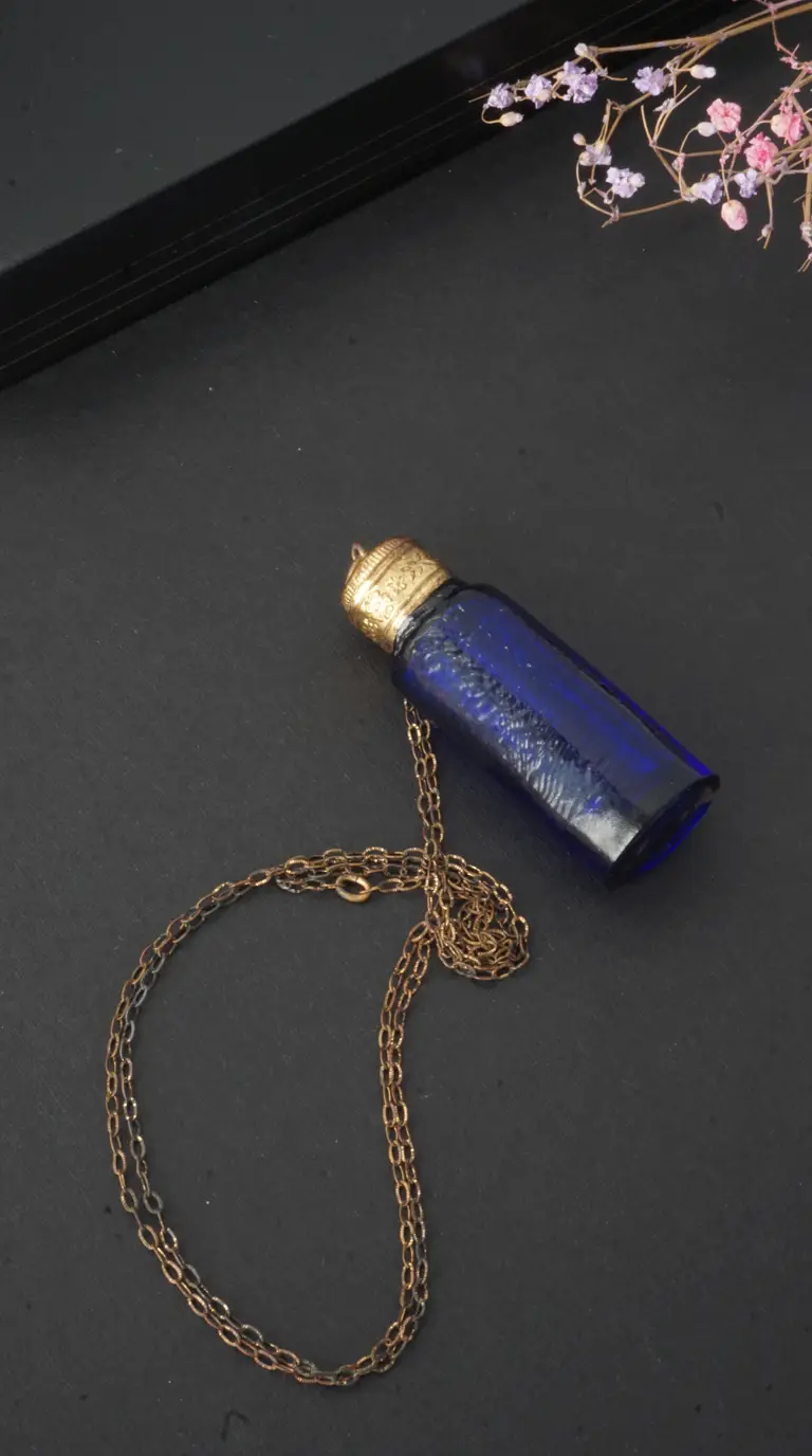Vintage blue glass perfume bottle pendant necklace with ornate gold-tone cap and delicate aged brass chain