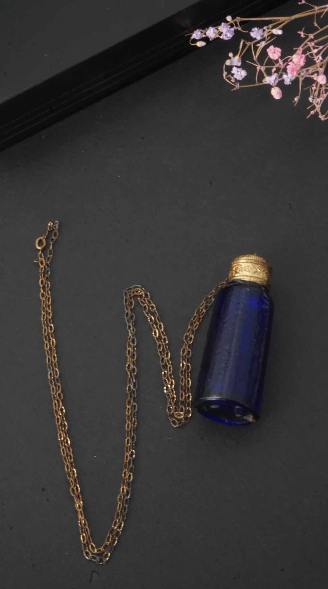 Vintage blue glass perfume bottle pendant necklace with ornate gold cap and delicate gold chain.