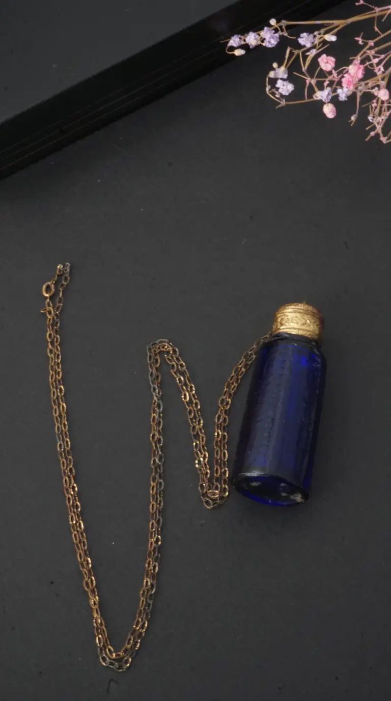Vintage blue glass perfume bottle pendant necklace with ornate gold cap and delicate gold chain.