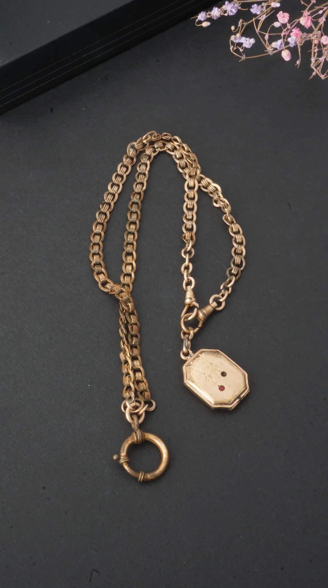 Vintage gold watch chain with engraved hexagonal locket, ruby, and black gemstone accents.