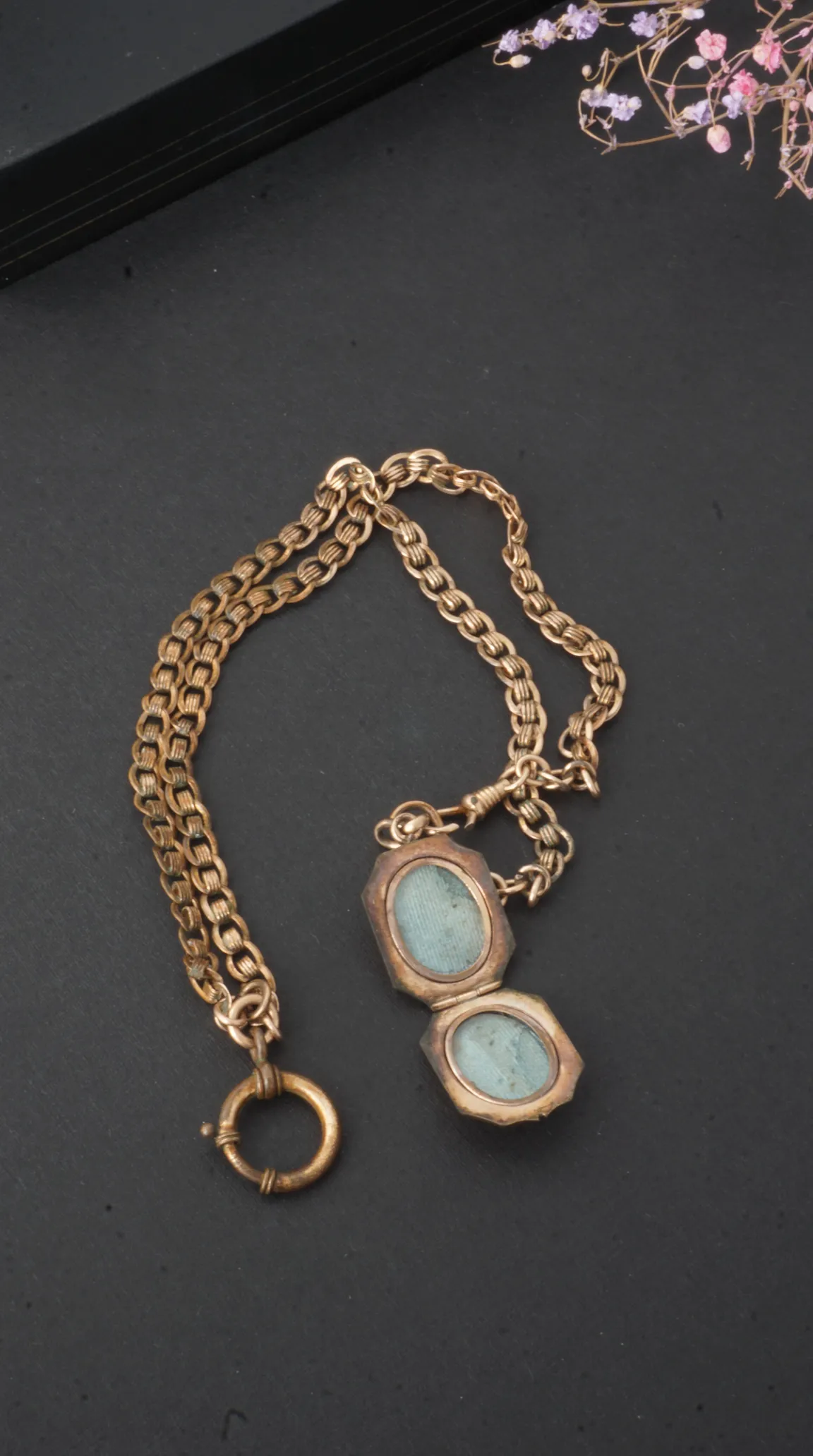 Vintage gold octagonal locket open with blue inserts on a textured chain against a dark background.